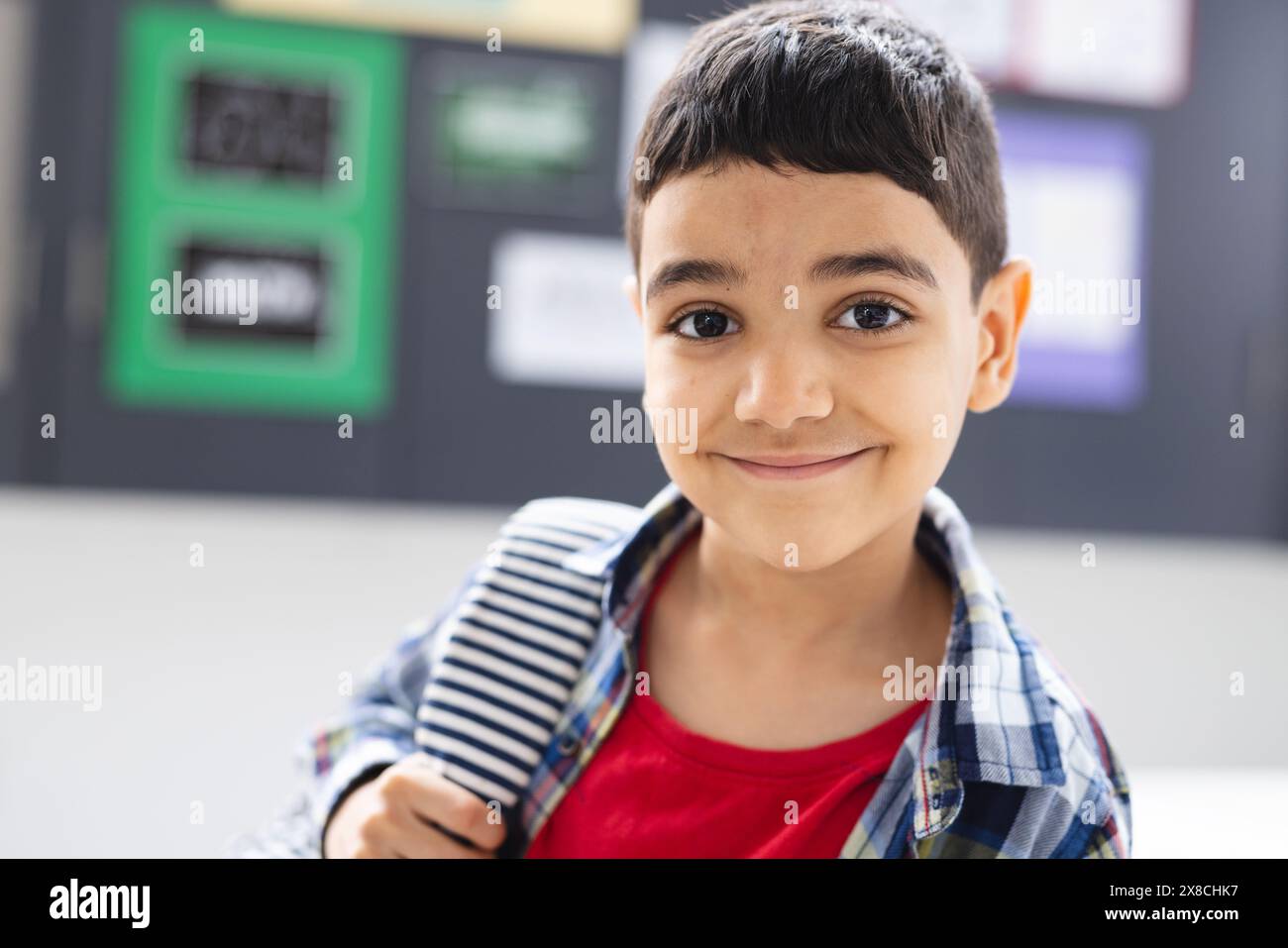 In der Schule lächelt ein junger birassischer Junge mit gestreiftem Rucksack im Klassenzimmer Stockfoto