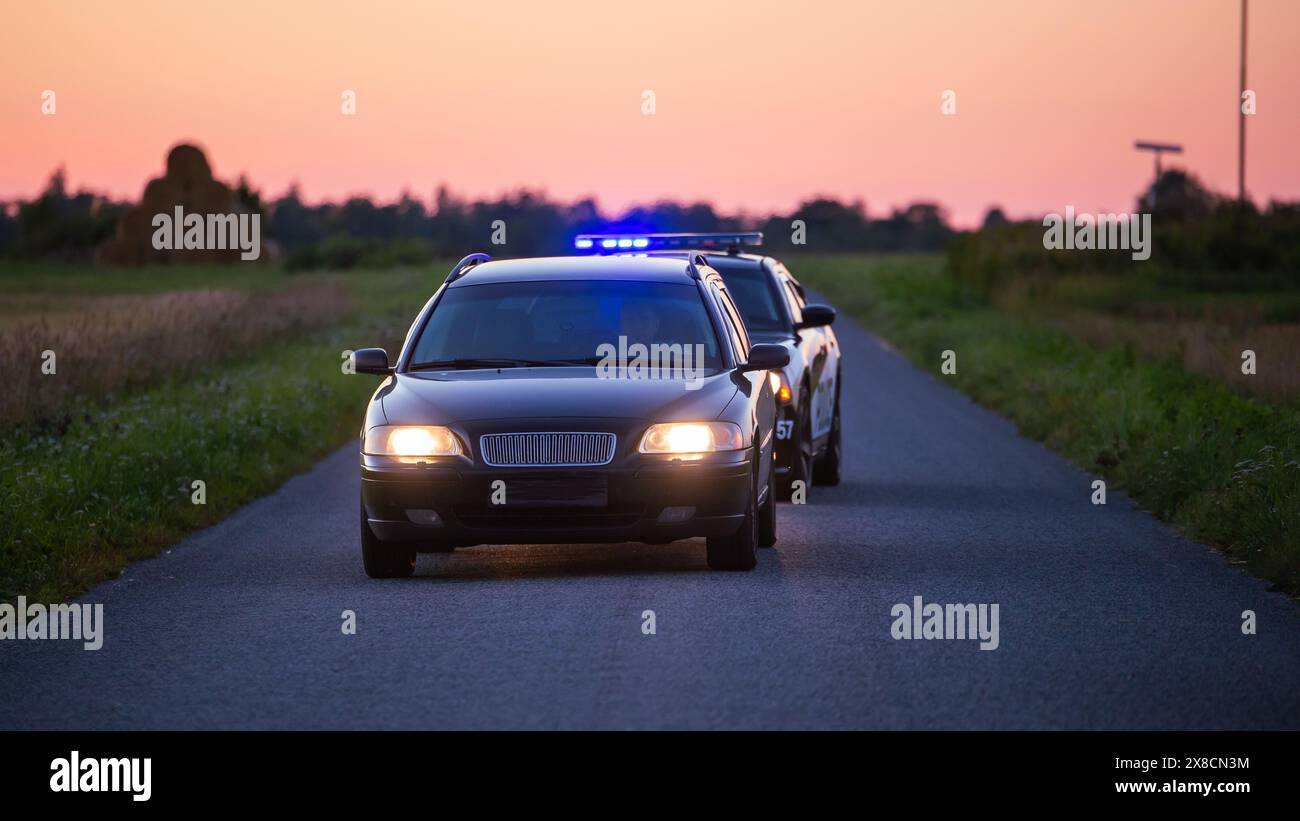 Highway Traffic Patrol Car verfolgt kriminelle Fahrzeuge, beschleunigt die Straße. Polizisten jagen Verdächtigen auf der Straße, Sirenen zünden, Dust Fying. Stilvolle Filmaufnahme mit energiegeladener Action-Szene Stockfoto