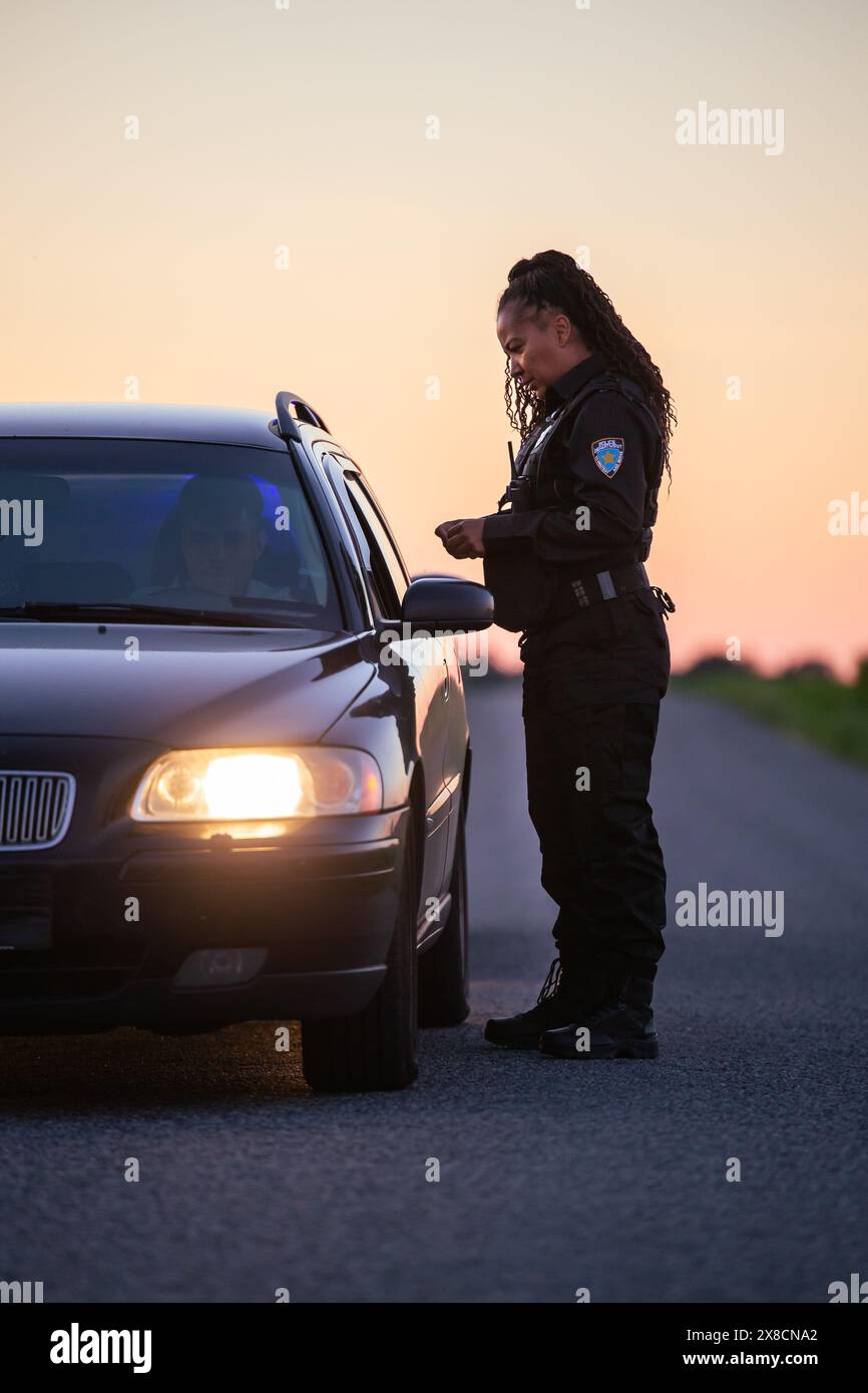 Highway Traffic Patrol Auto fahren, Routine Check, Road Inspection Stop. Professionelle schwarze Polizistin nähert sich dem Fahrzeug, fragt nach Führerschein und Zulassung. Kinofilm Stockfoto