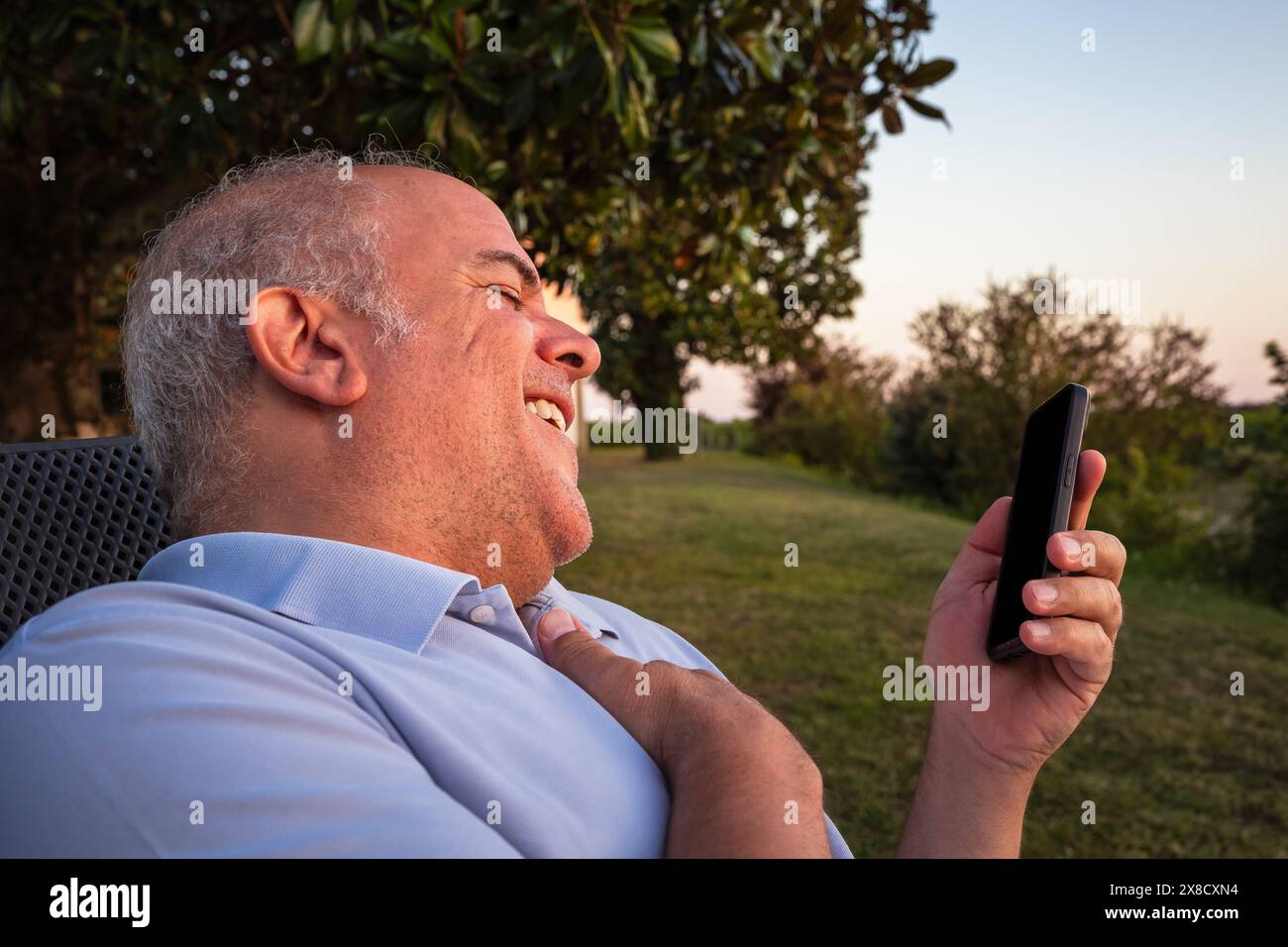 Erwachsener weißer Mann, der im Garten ruht, mit Handy in der Hand, das bei Sonnenuntergang spricht Stockfoto