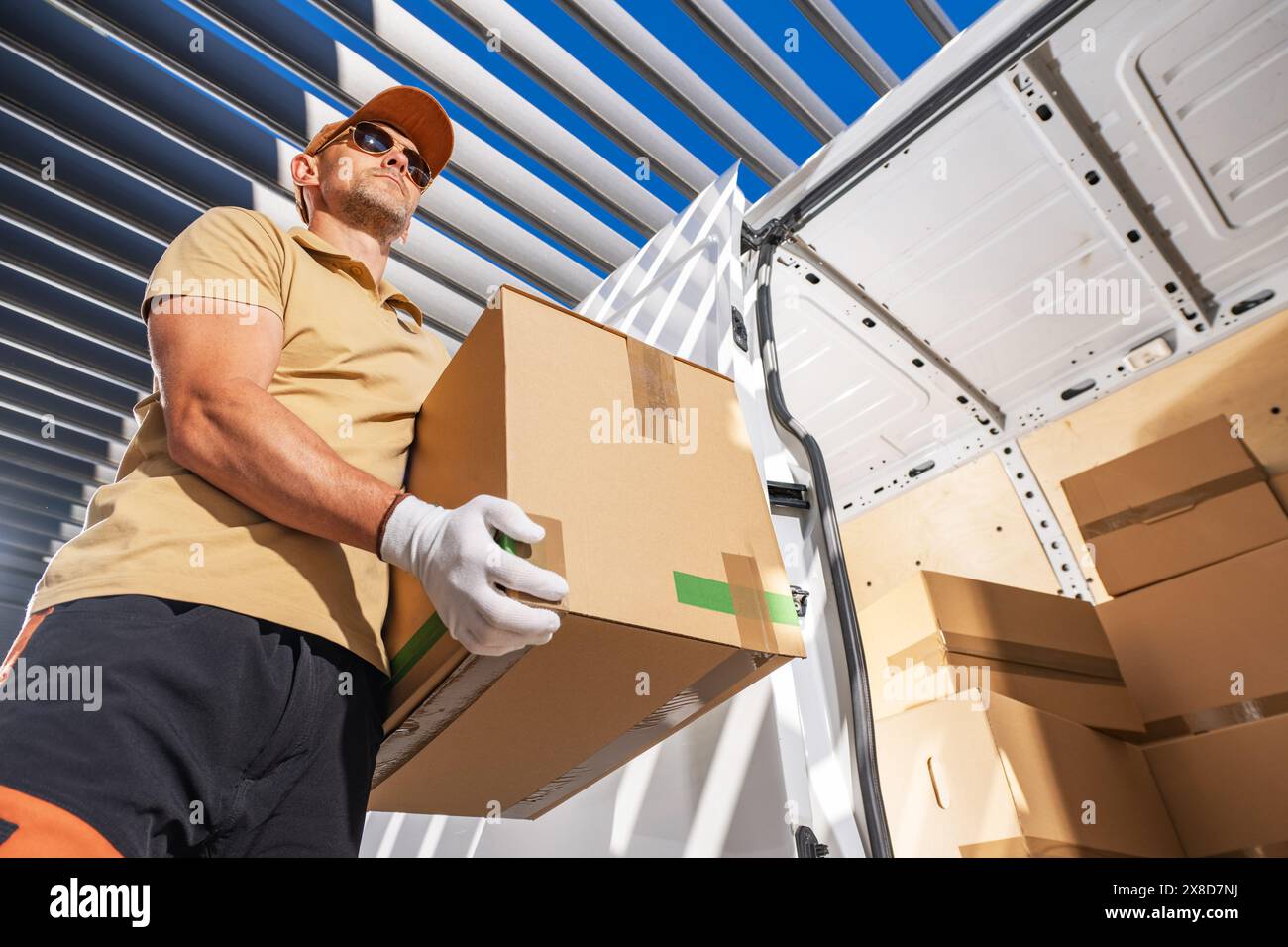 Ein Kurier in einem gelben Hemd und weißen Handschuhen hält eine Kiste mit einem ernsthaften Gesichtsausdruck. Stockfoto