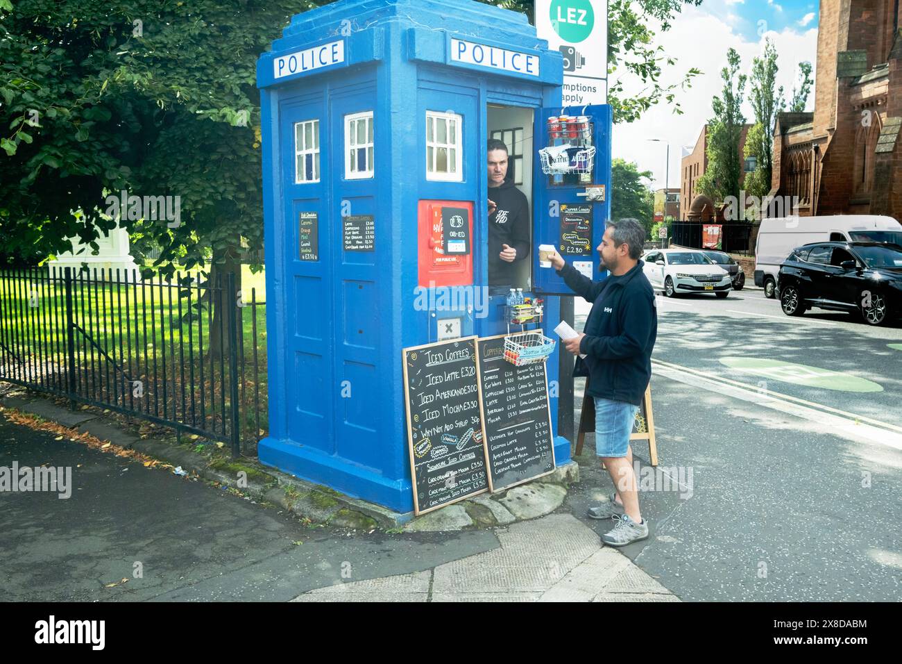 Ein männlicher Erwachsener steht neben einer tardis-Polizeibox, die auch als Menütafel in der City Street in Glasgow, Schottland, dient Stockfoto