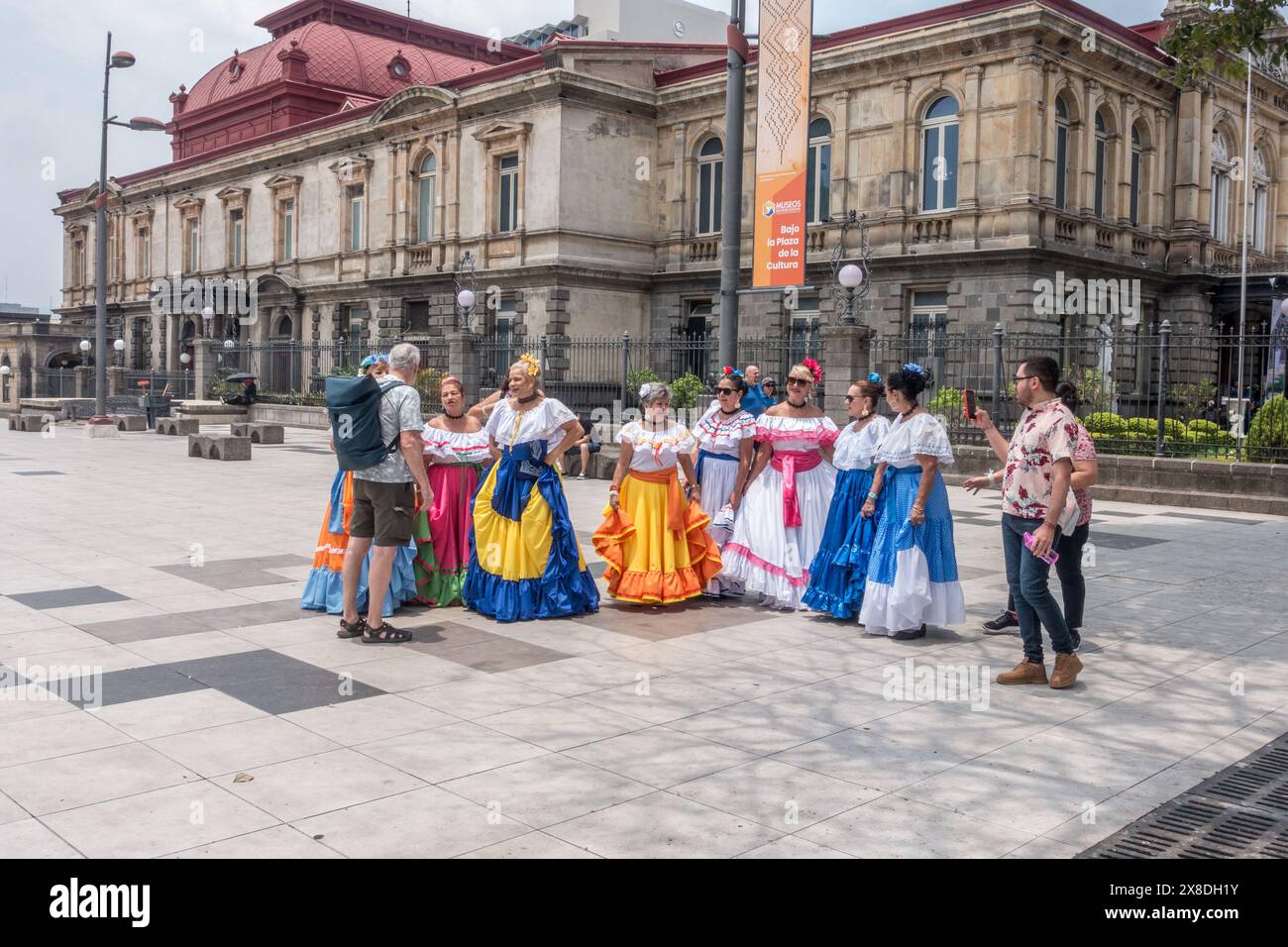 Ein neugieriger Mann spricht mit einer Gruppe älterer Frauen in traditionellen Costa-ricanischen Kleidern vor dem Nationaltheater in San José, Costa Rica. Stockfoto
