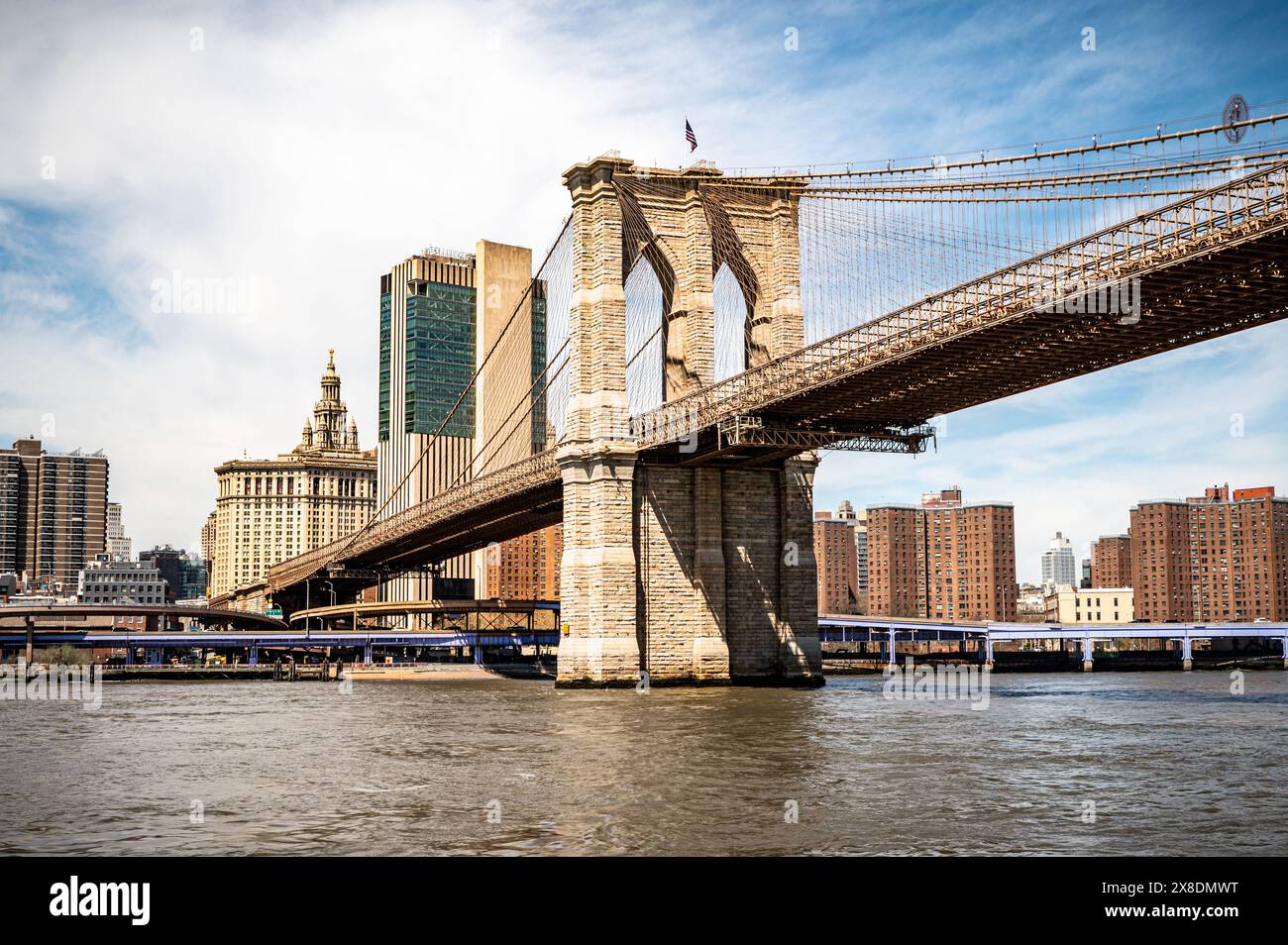 Die majestätische Brooklyn Bridge ziert die Skyline von New York City. Hoch aufragende Stahlbögen umrahmen das Stadtbild, in warmes Sonnenlicht getaucht. Legendäres Wahrzeichen für Reisen. Stockfoto