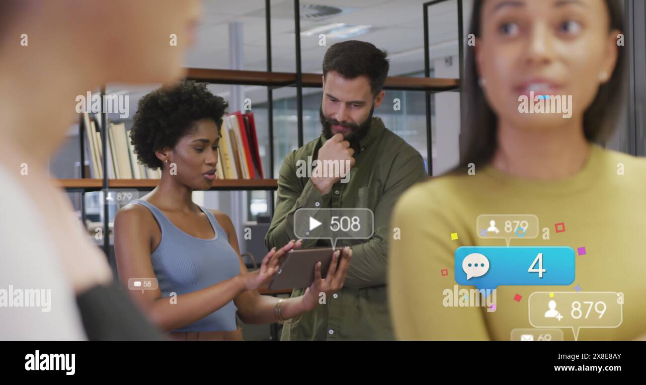 Bild von Social-Media-Ikonen über verschiedene Männer und Frauen, die im Büro über ein digitales Tablet diskutieren Stockfoto