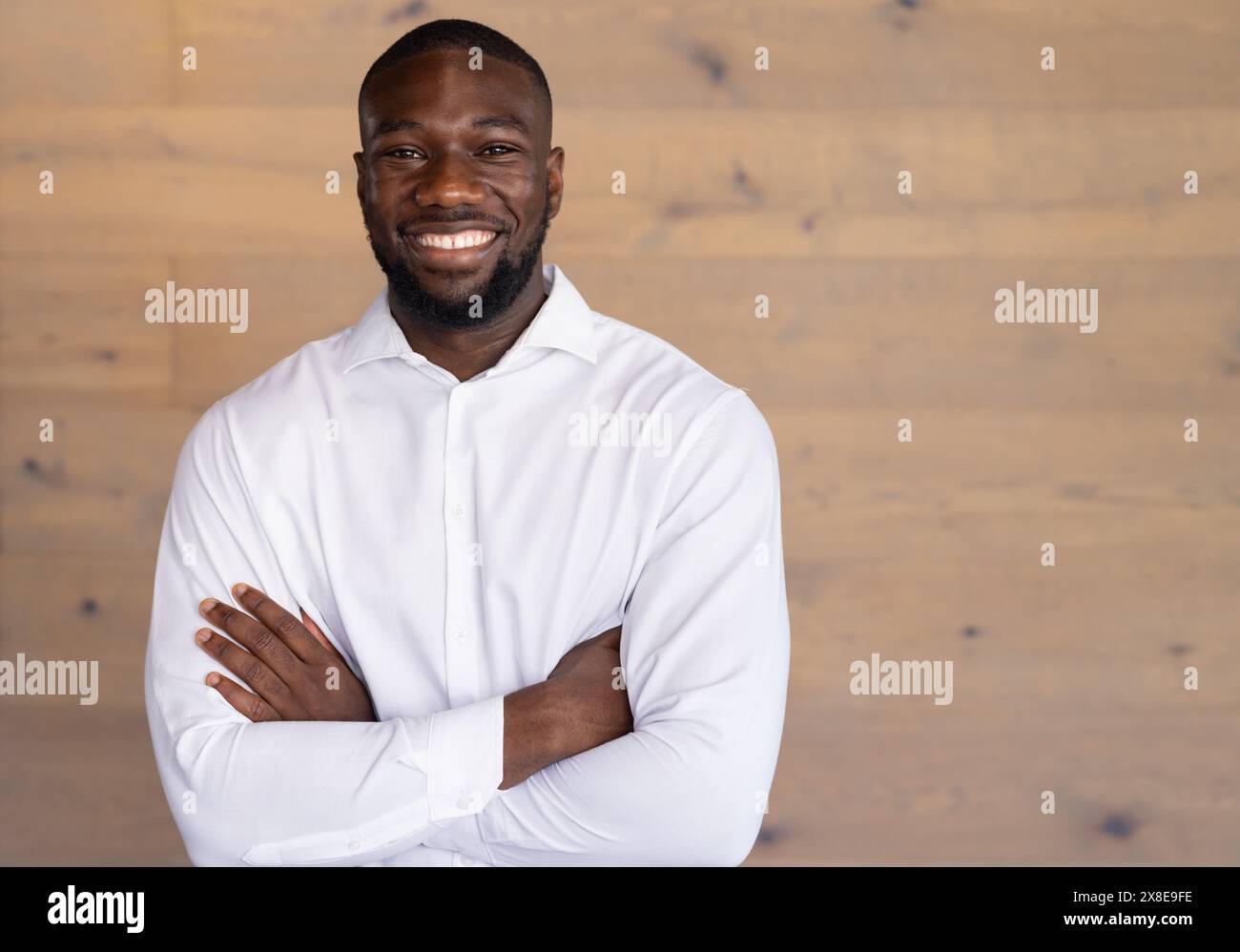 In einem modernen Büro steht ein junger Afroamerikaner mit überkreuzten Armen und lächelndem Kopierraum Stockfoto