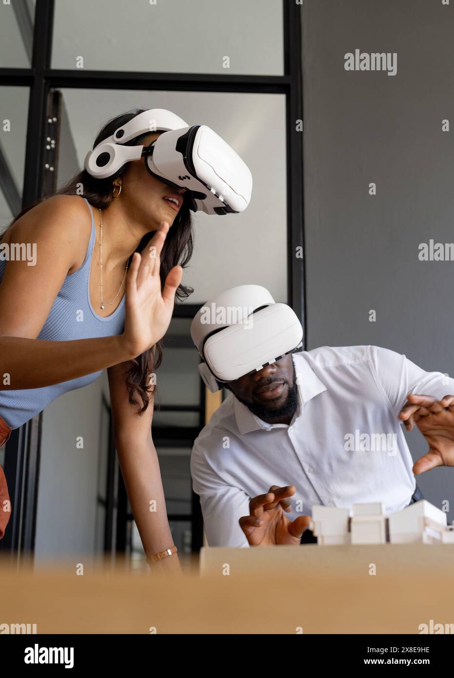 Vielseitiges Team mit Virtual-Reality-Headsets in modernen Büros. Junge afroamerikanische männliche Kollegin und junge indische Teamleiterin interagieren mit wi Stockfoto