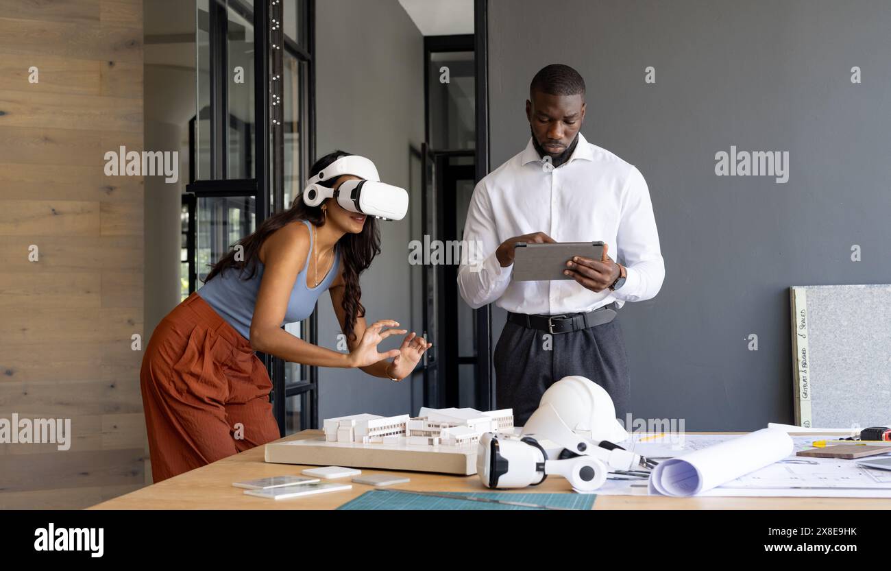 In modernen Büros arbeitet ein vielseitiges Team an Architekturprojekten. Junger afroamerikanischer Kollege, der ein Tablet benutzt, während der junge indische Teamleiter erforscht Stockfoto