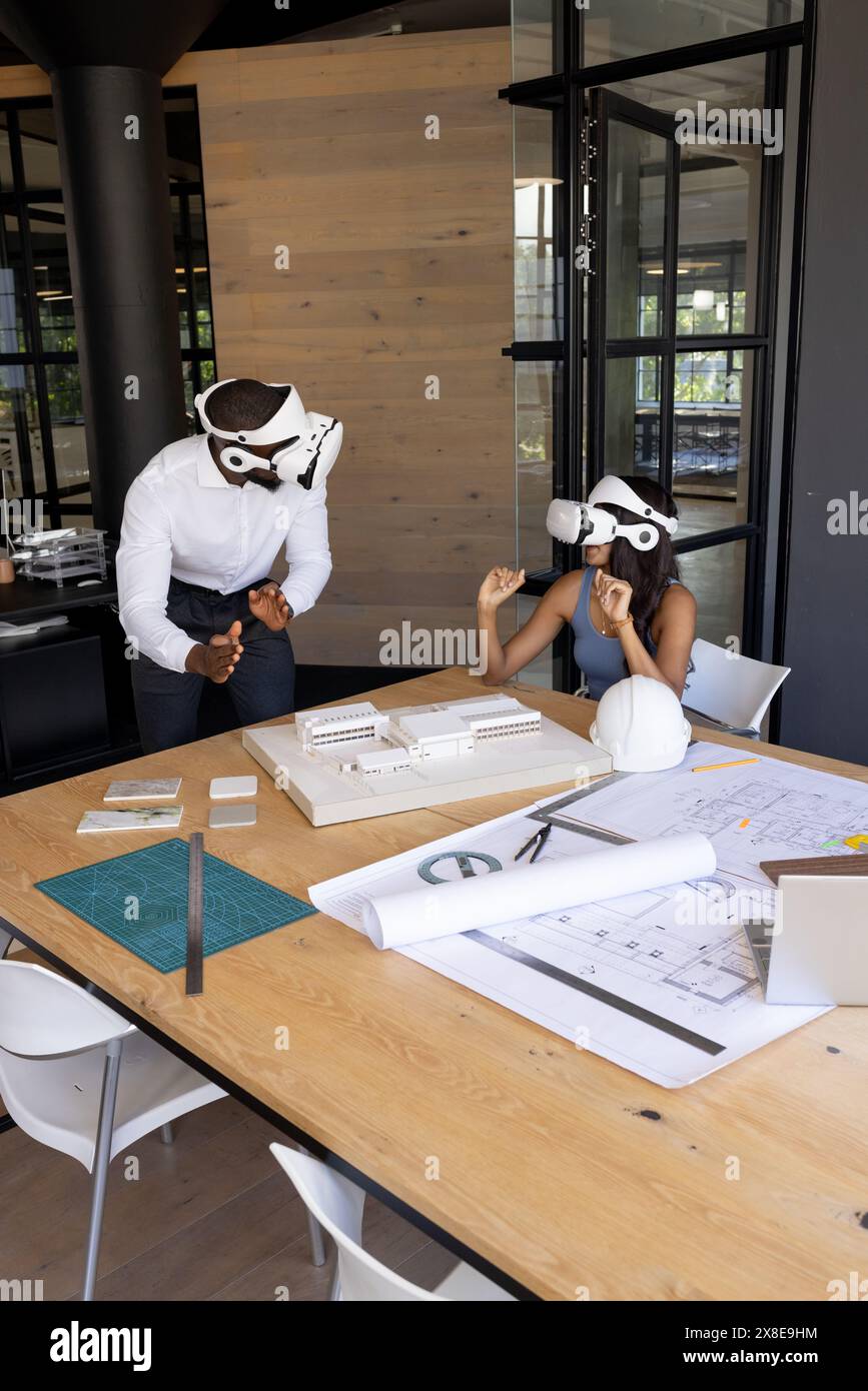 Junges, vielfältiges Team im Büro, das VR-Headsets verwendet und mit virtuellen Modellen interagiert. Afroamerikaner in weißem Hemd und indische Frau in schwarzen Dres Stockfoto