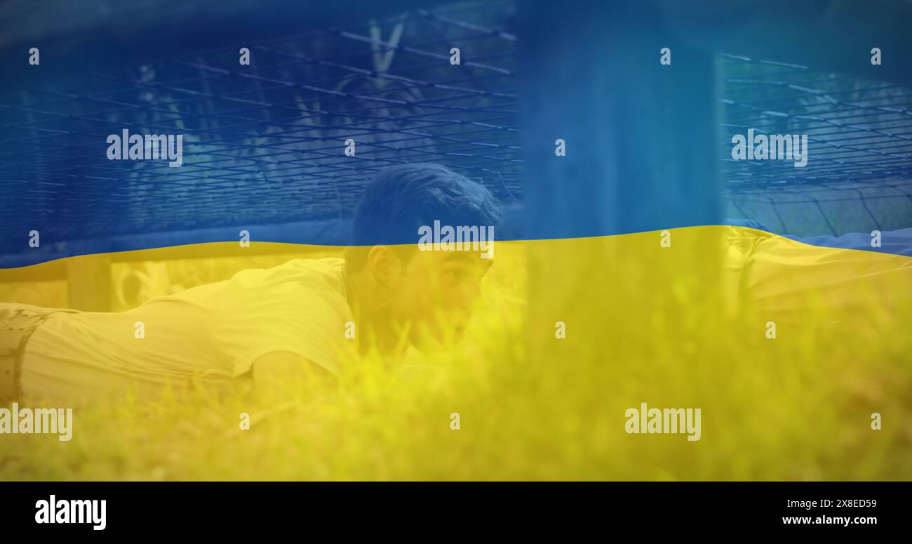 Kaukasischer Profi in Gelb, liegt auf Gras und blickt durch eine ukrainische Flagge Stockfoto