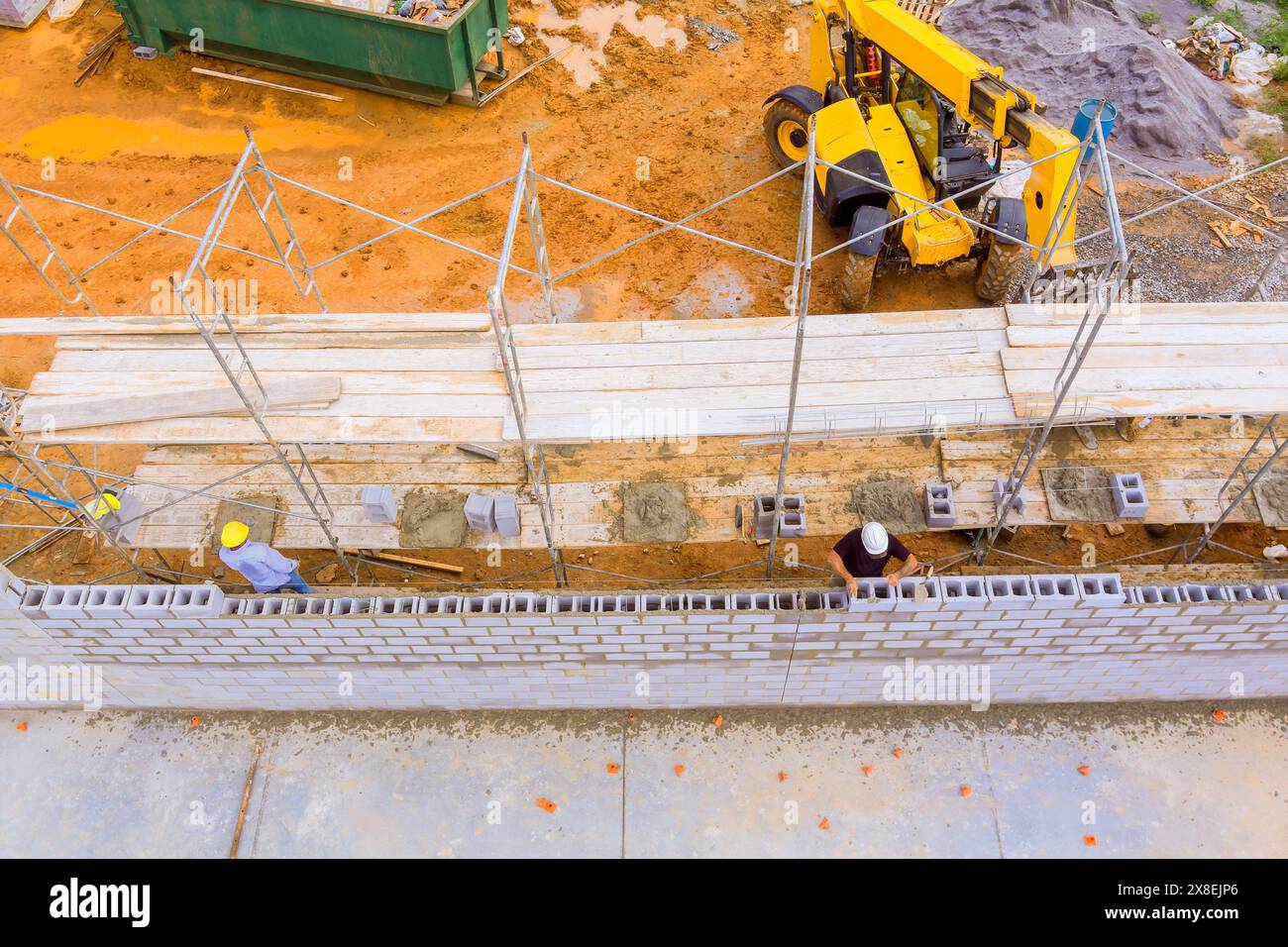 Maurer baut eine funktionierende Betonwand aus Betonblöcken, während er auf Gerüsten steht Stockfoto