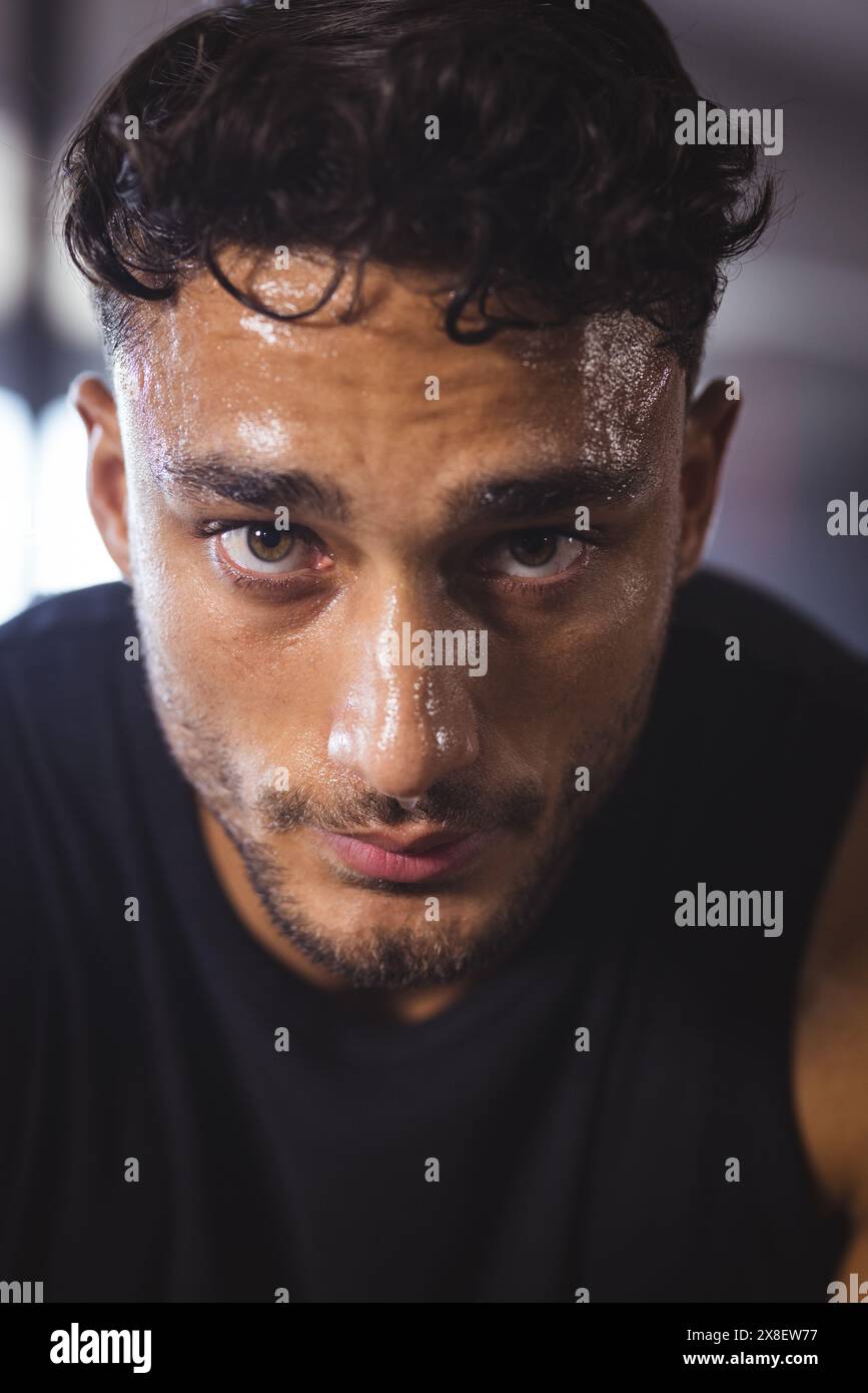 Im Fitnessstudio schwitzt ein starker und fitter birassischer Mann nach intensivem Training. Fitnessgeräte und Gewichte im Hintergrund sichtbar, schaffen eine fokussierte Atmosphäre, unal Stockfoto