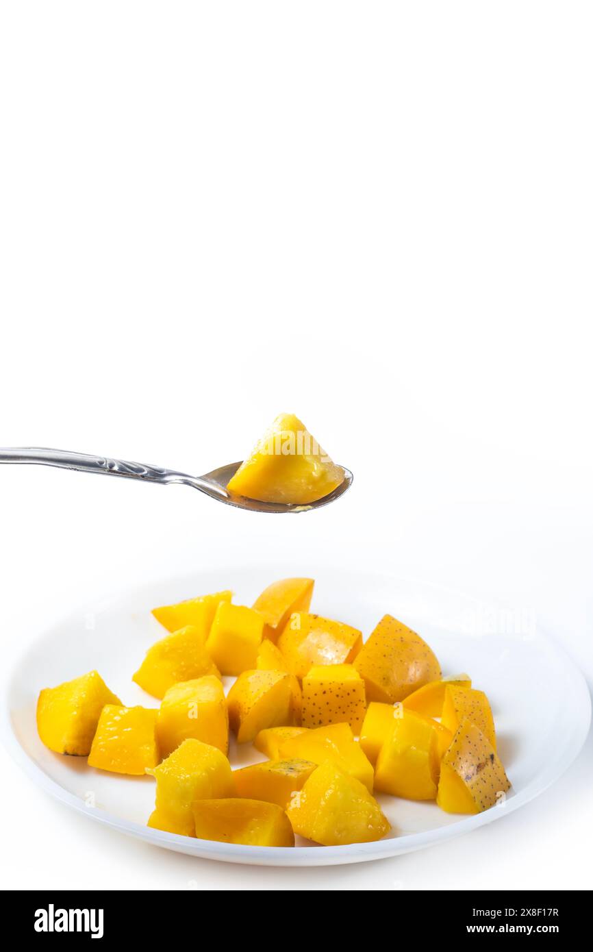 Mangoscheiben auf weißer Platte mit Löffel isoliert auf weißem Hintergrund. Vertikale Aufnahme. Stockfoto