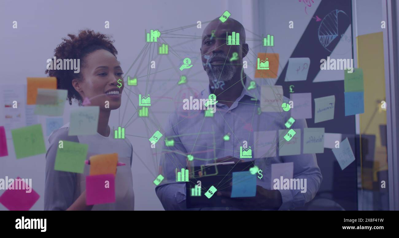 Bild einer Welt der Finanzsymbole über afroamerikanischen Mann und Frau, die über Memo-Notizen diskutieren Stockfoto