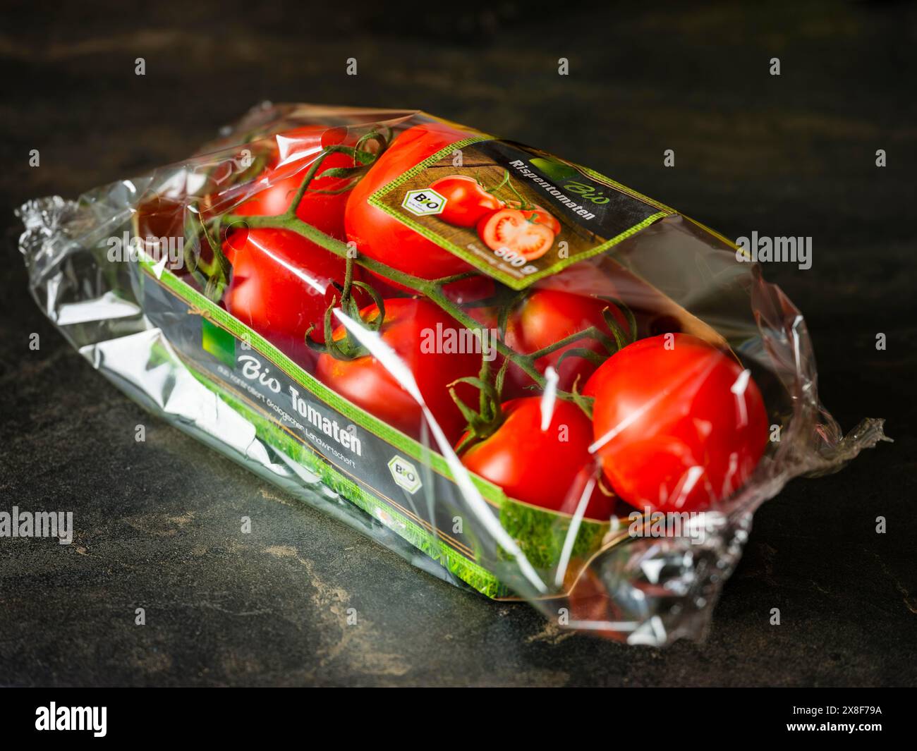 Reife Tomaten aus roter Weinrebe mit grünen Stielen in Kunststoffverpackung mit organischer Versiegelung Stockfoto