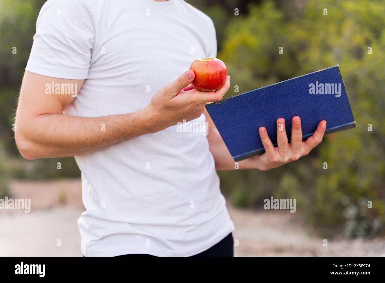 Nahaufnahme eines Mannes, der ein Buch und einen Apfel als Konzept für ein gesundes Gleichgewicht zwischen Geist und Körper hält Stockfoto