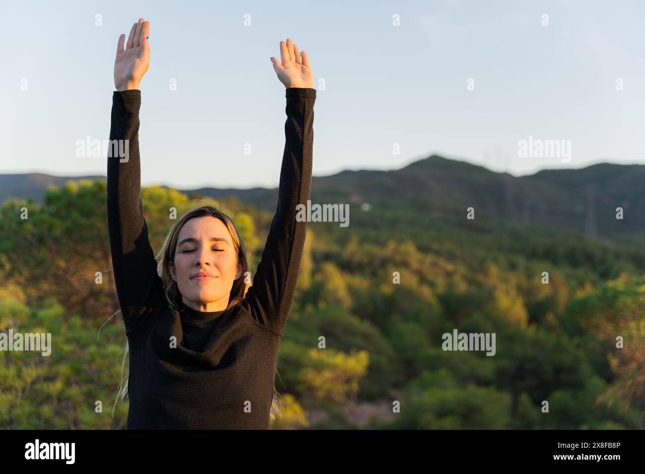 Porträt einer lächelnden Frau, die am frühen Morgen ihre Arme streckt. Innere Ruhe und geistiges Wohlbefinden Stockfoto
