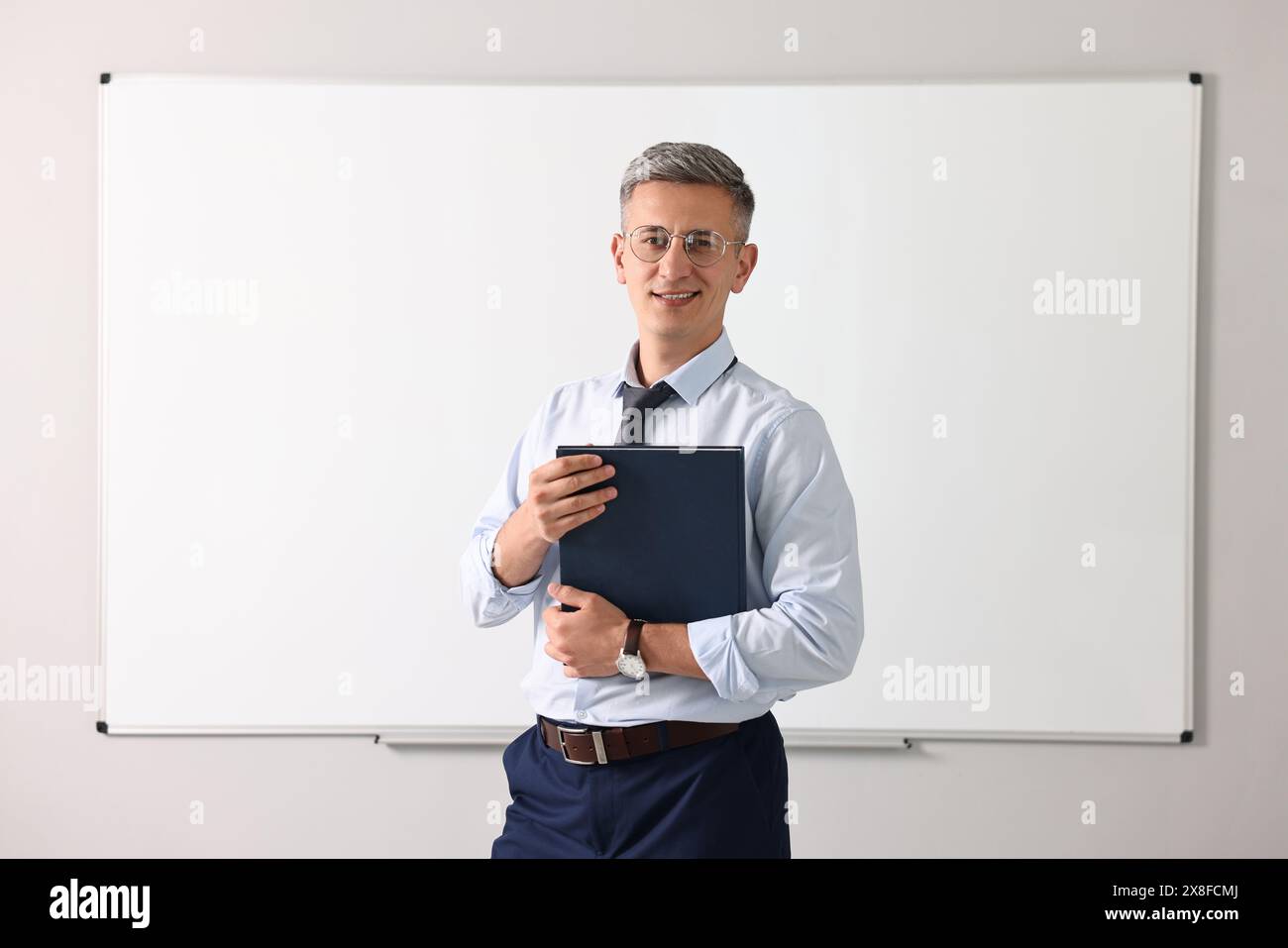 Lehrer mit Notizbuch in der Nähe des Whiteboards im Klassenzimmer Stockfoto