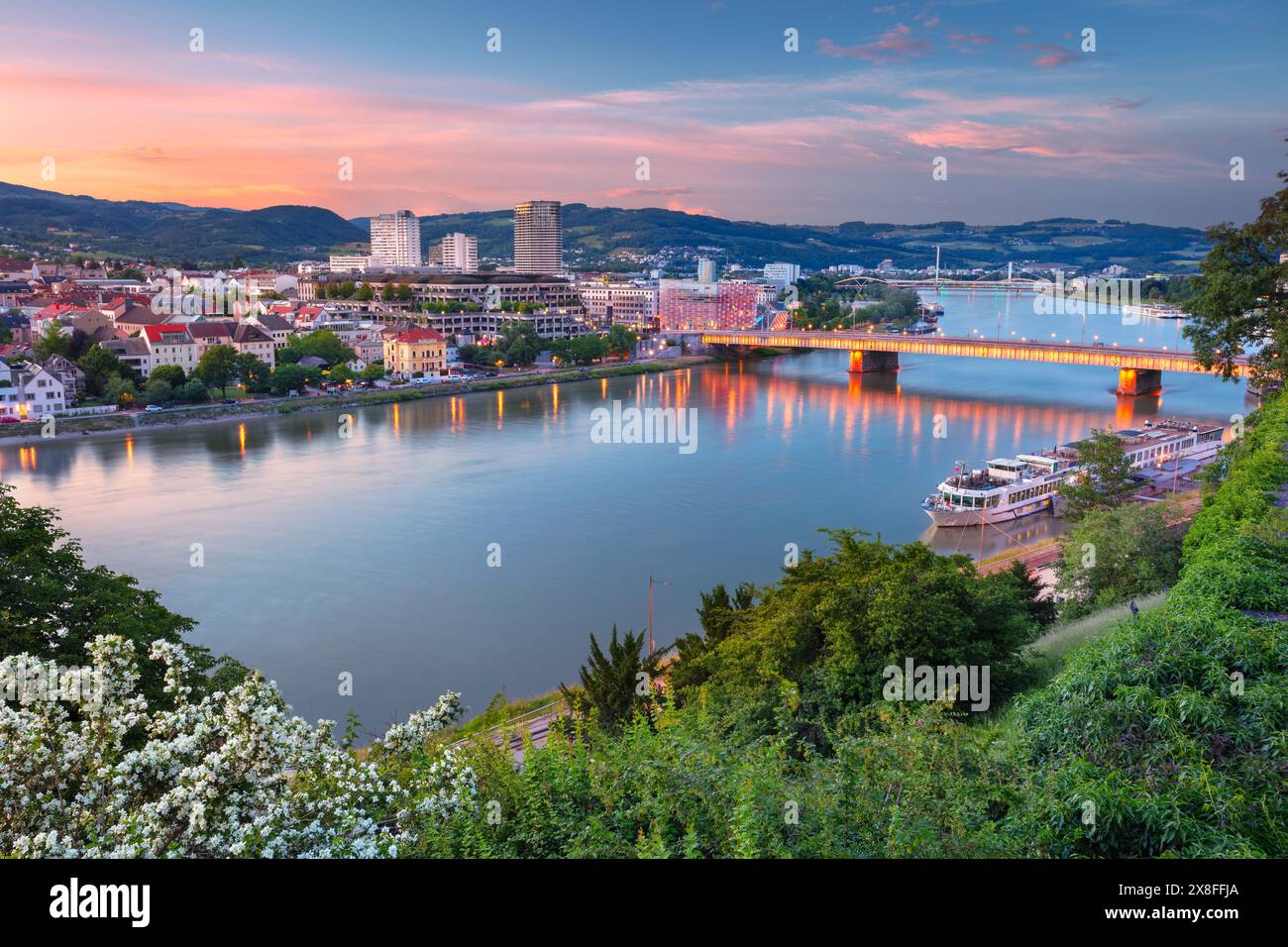 Linz, Österreich. Luftbild des Flusses Linz, Österreich während des Frühlingsuntergangs mit Reflexion der Stadtlichter in der Donau. Stockfoto