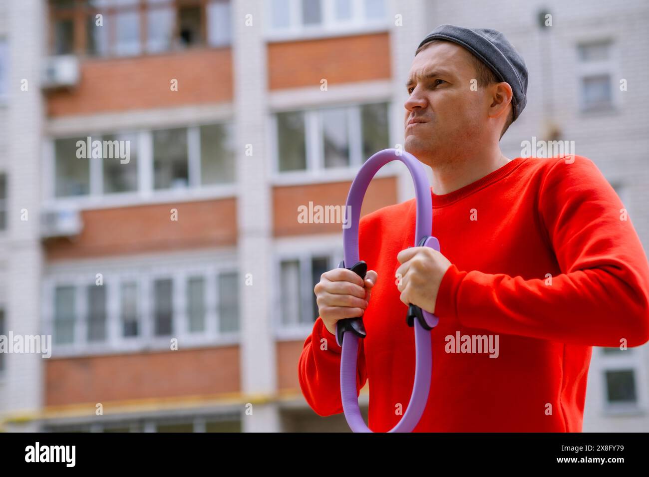 Ein Sportler in einem roten Hemd hält einen violetten Ring-Expander für Pilates, während er Aerobic trainiert. Stockfoto