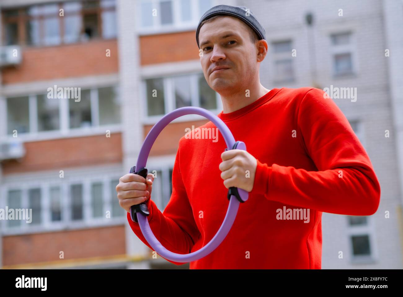 Ein Sportler in einem roten Hemd hält einen violetten Ring-Expander für Pilates, während er Aerobic trainiert. Stockfoto