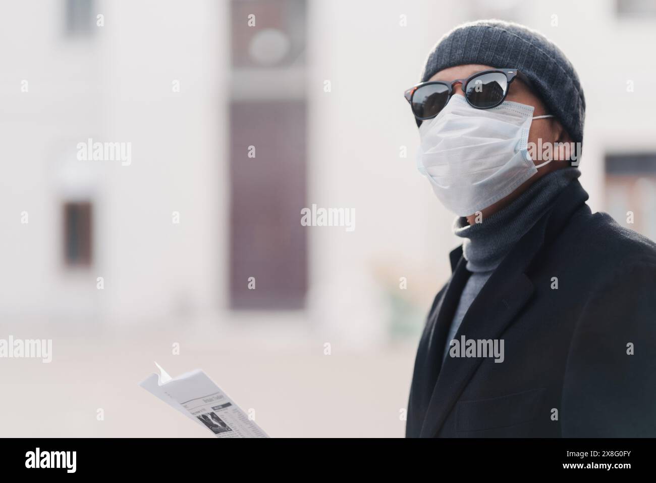 Ein Stadtforscher in Maske und Sonnenbrille schaut diskret seine Zeitung. Stockfoto