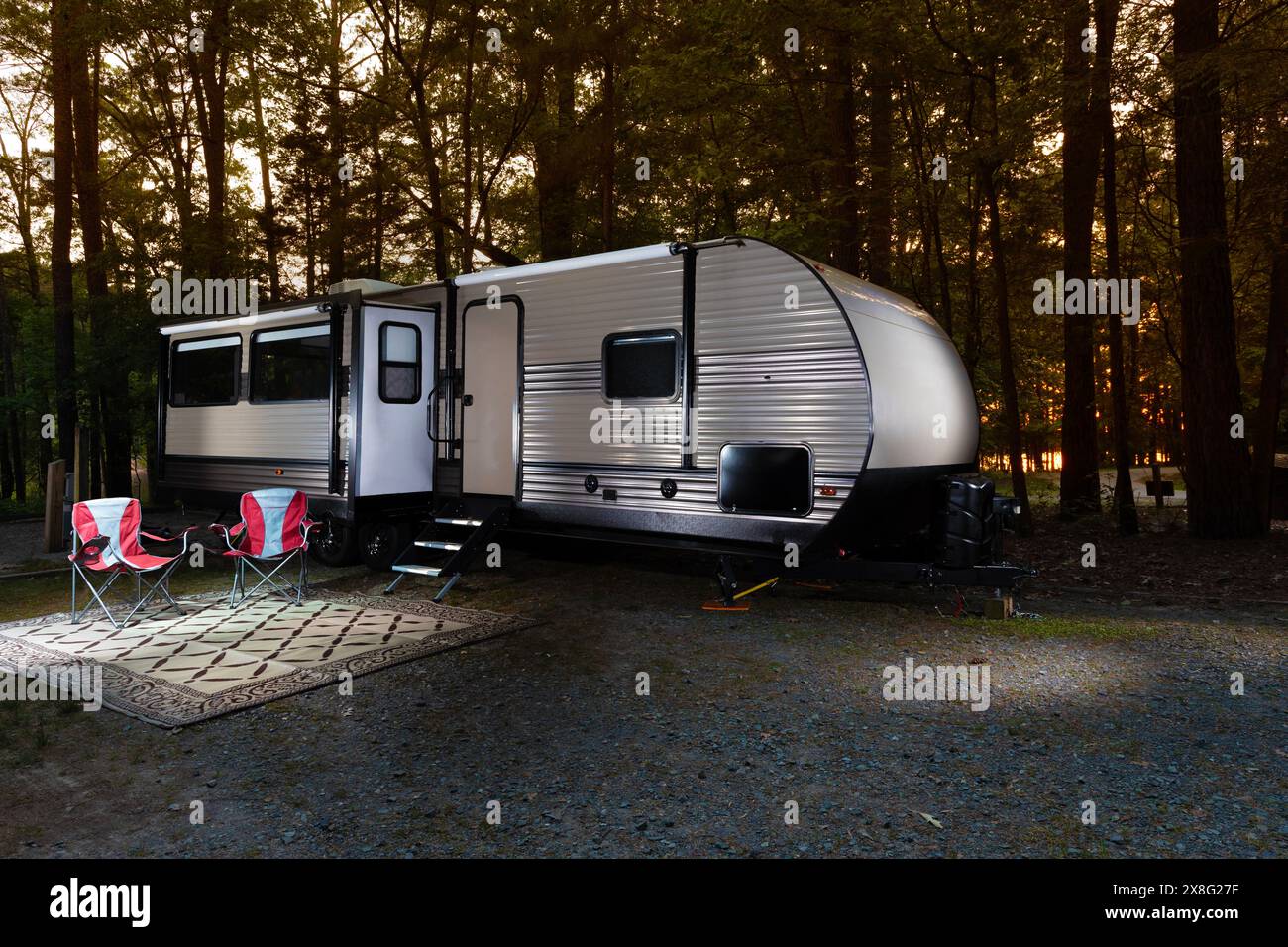 Rote Stühle vor einem Wohnmobil bei Sonnenuntergang auf einem bewaldeten Campingplatz Stockfoto