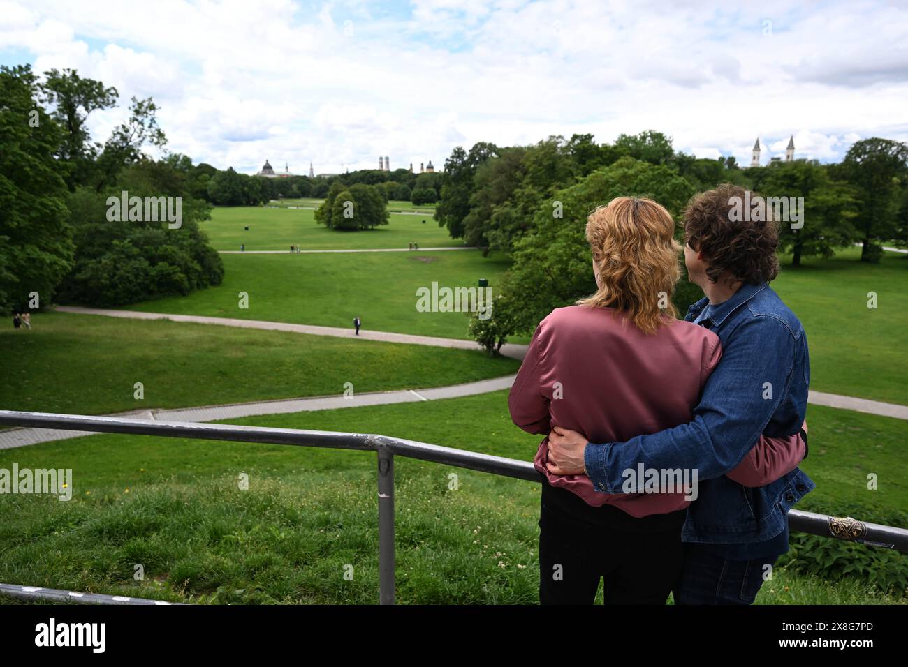 München, Deutschland. Mai 2024. Nadja (l) und Faustus entspannen sich im Englischen Garten auf den Monopteros und blicken in Richtung Stadtzentrum mit Frauenkirche und Staatskanzleramt, um sich von ihrem Besuch beim Metallica-Konzert zu erholen. Am Sonntag besuchen die beiden das zweite Konzert der Rockband. Quelle: Felix Hörhager/dpa/Alamy Live News Stockfoto