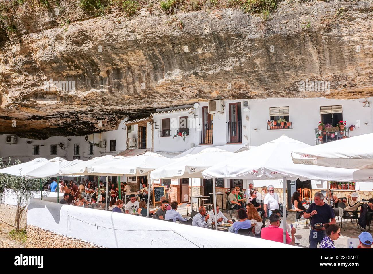 Restaurants und Cafés drängen sich unter einem Felsüberhang entlang der Terrazas Calle Cuevas del Sol in den einzigartigen Pueblos blanco von Setenil de las Bodegas, Spanien. Die Bewohner des kleinen Dorfes Setenil leben seit dem neolithikum in Höhlenhäusern. Stockfoto