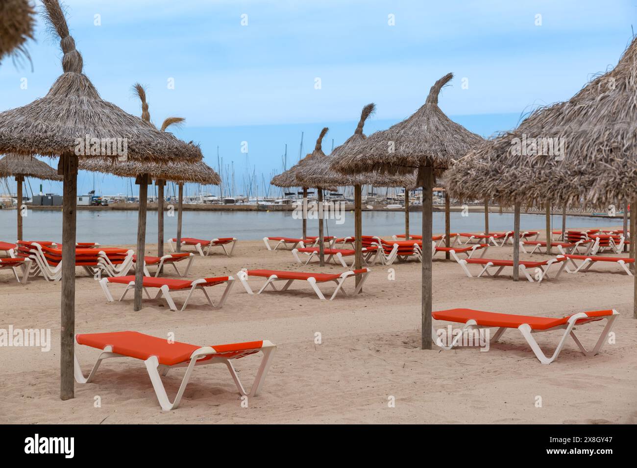 Leerer Sandstrand, rote Sonnenliegen, Strohschirme, Meer, Sommerzeit Stockfoto