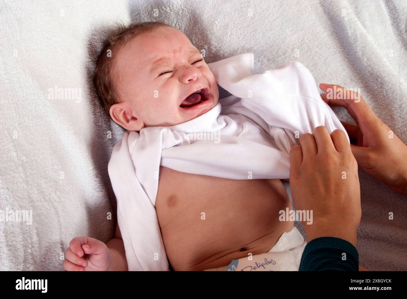 Baby weint, als Mutter versucht, ihn anzuziehen Stockfoto