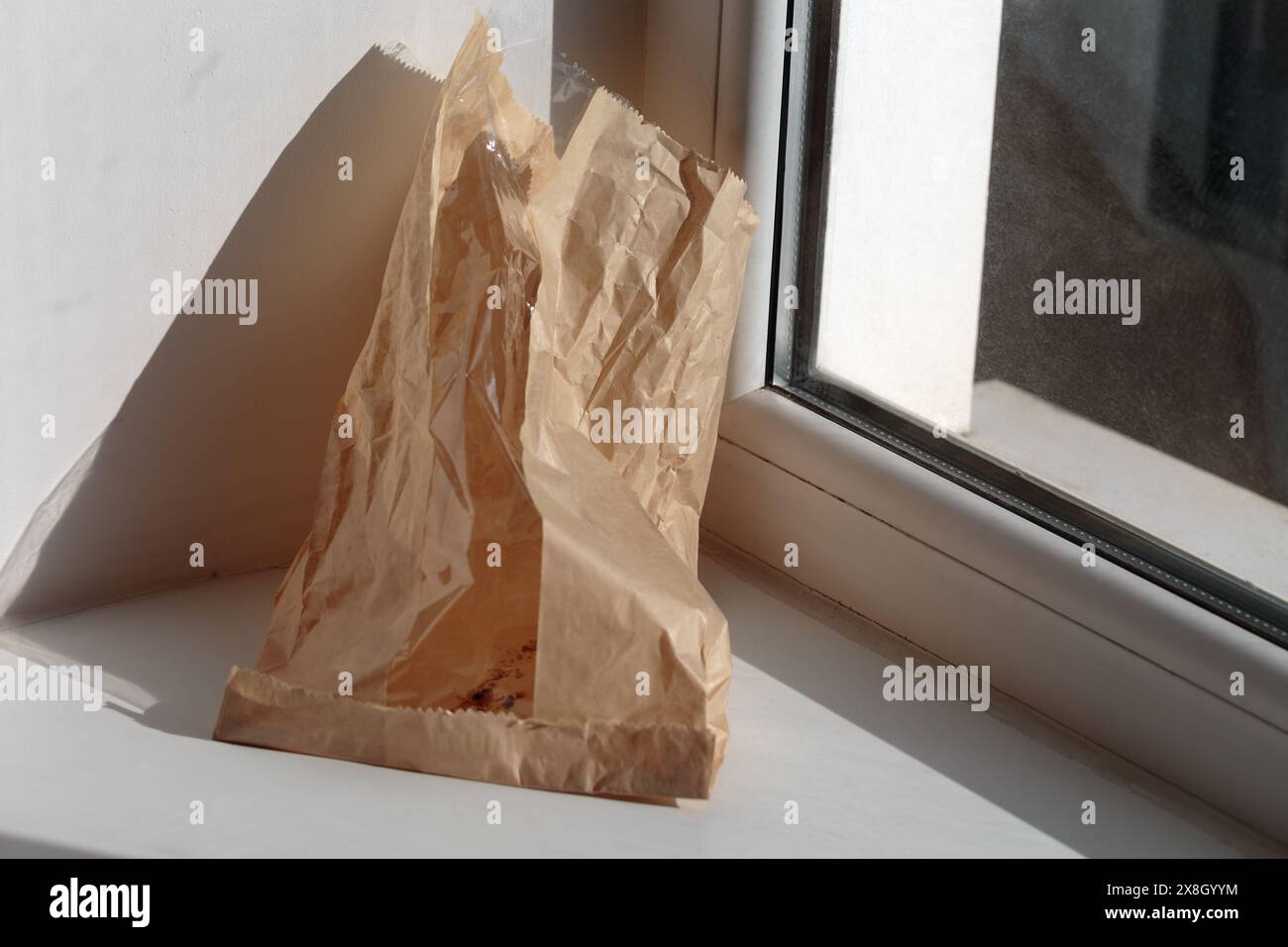 Eine Papiertüte unter einem Brötchen mit Sesamsamen auf einer weißen Fensterbank. Platzieren für Ihren Text. Nahaufnahme. Stockfoto Eine Papiertüte unter einem Brötchen mit Sesamsamen auf einer weißen Fensterbank. Platzieren für Ihren Text. Nahaufnahme. Stockfoto