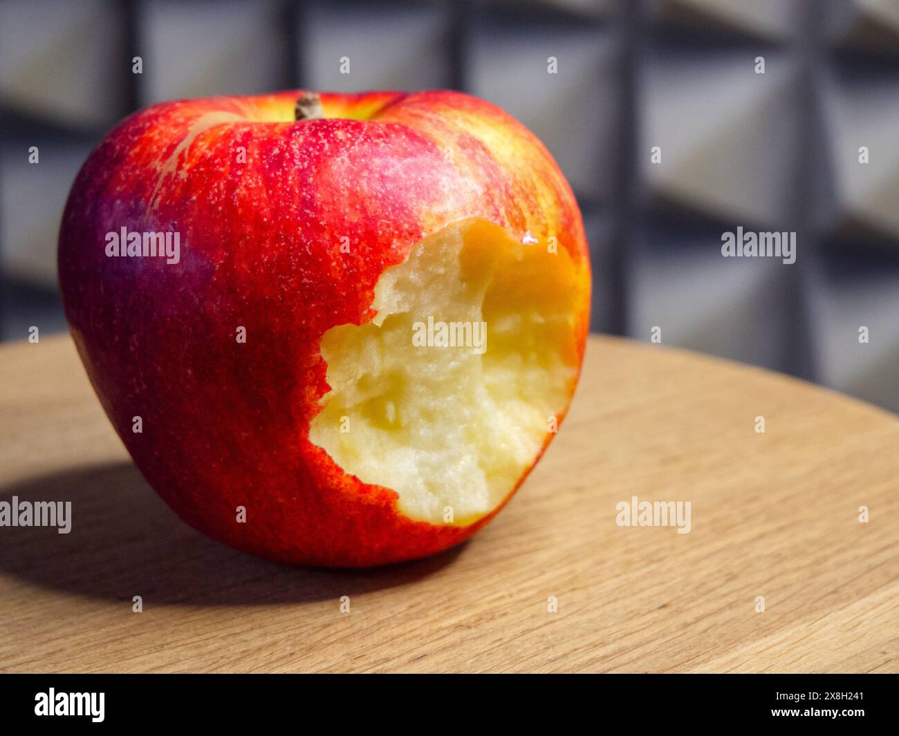 Apfel auf Holztisch gegessen. Ein Apfel mit Bissspur auf einem Holztisch, geeignet für Themen der Ernährung und des natürlichen Lebensstils. Stockfoto