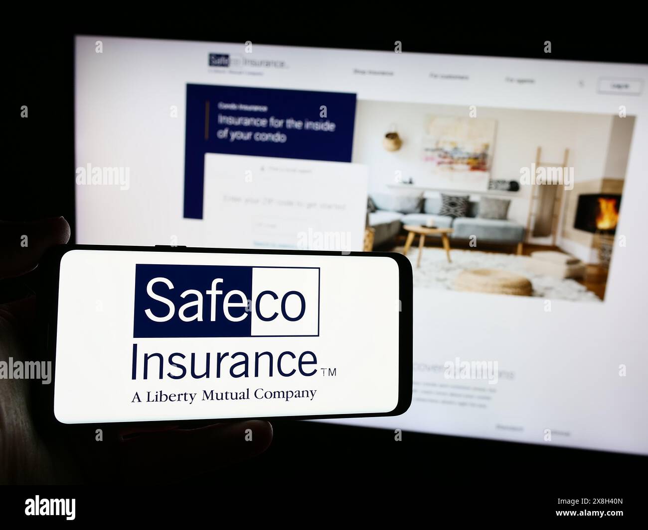 Person mit Smartphone und Logo des US-Finanzdienstleisters Safeco Insurance vor der Website. Schwerpunkt auf dem Display des Telefons. Stockfoto