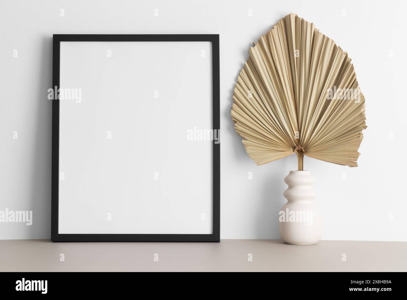 Schwarzes Rahmenmockup mit Palmblattdekoration auf dem beigefarbenen Tisch. Stockfoto