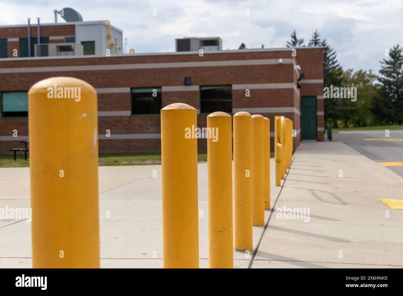 Gelbe Poller standen vor einem Backsteingebäude - industrielle Elemente sichtbar - unter einem teilweise bewölkten Himmel. Aufgenommen in Toronto, Kanada. Stockfoto