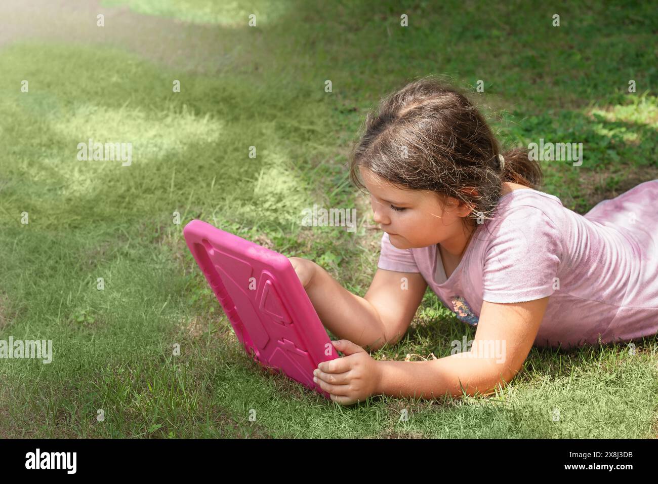 Ein Kind benutzt eine Tablette auf dem Gras im Garten Stockfoto