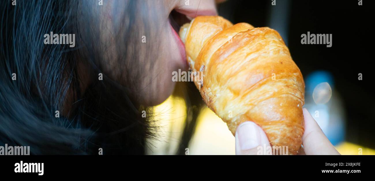 Nahaufnahme einer Person, die ein Croissant isst, wobei der Schwerpunkt auf das Gebäck und den Mund der Person liegt. Stockfoto