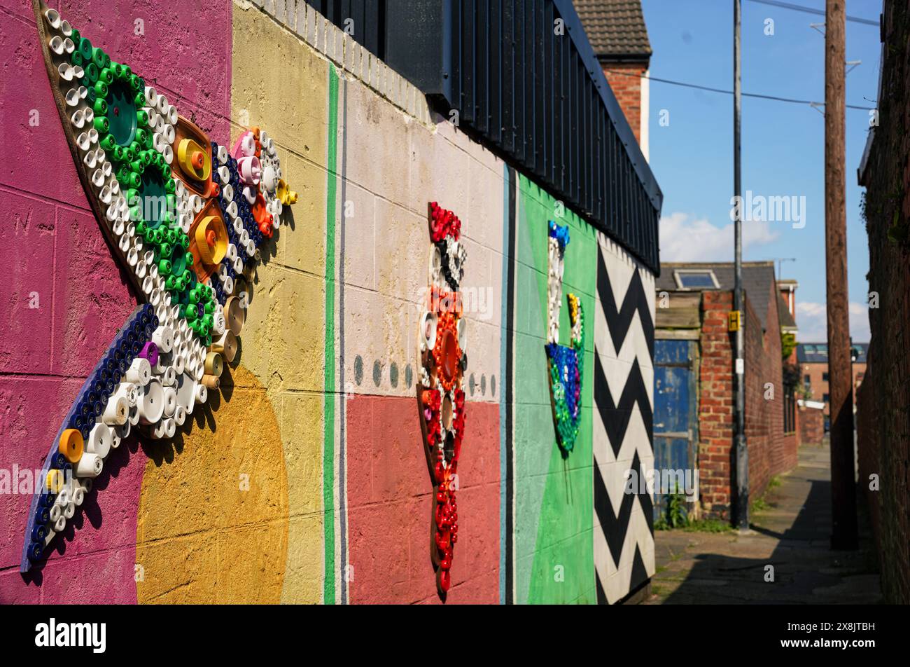 Farbenfrohe Kunstwerke aus Plastikflaschen, die an bemalten Wänden in einer Gasse in Whitley Bay befestigt sind Stockfoto