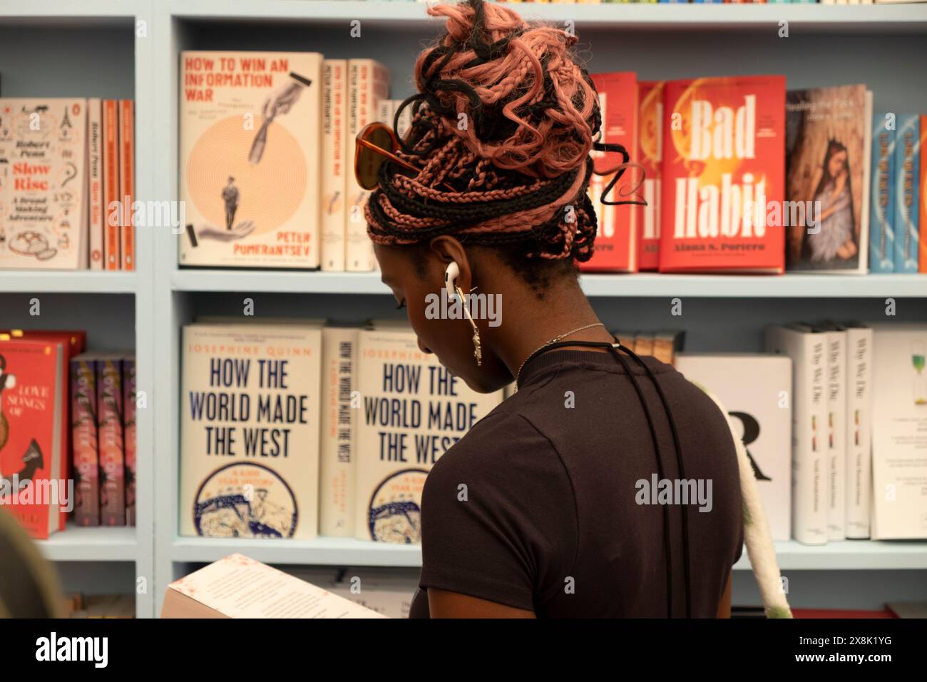 Person junge Frau Leserin rückwärtige Lektüre, die Bücher zum Verkauf in Bücherregalen im Buchladen beim Hay Festival 2024 Hay-on-Wye UK ansieht KATHY DEWITT Stockfoto