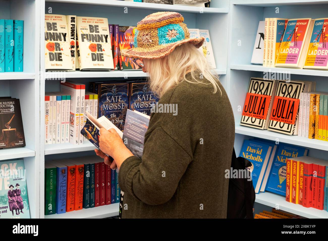 Person ältere Frau Strohhut Leserin liest Bücher zum Verkauf in Bücherregalen im Buchladen beim Hay Festival 2024 Hay-on-Wye UK KATHY DEWITT Stockfoto
