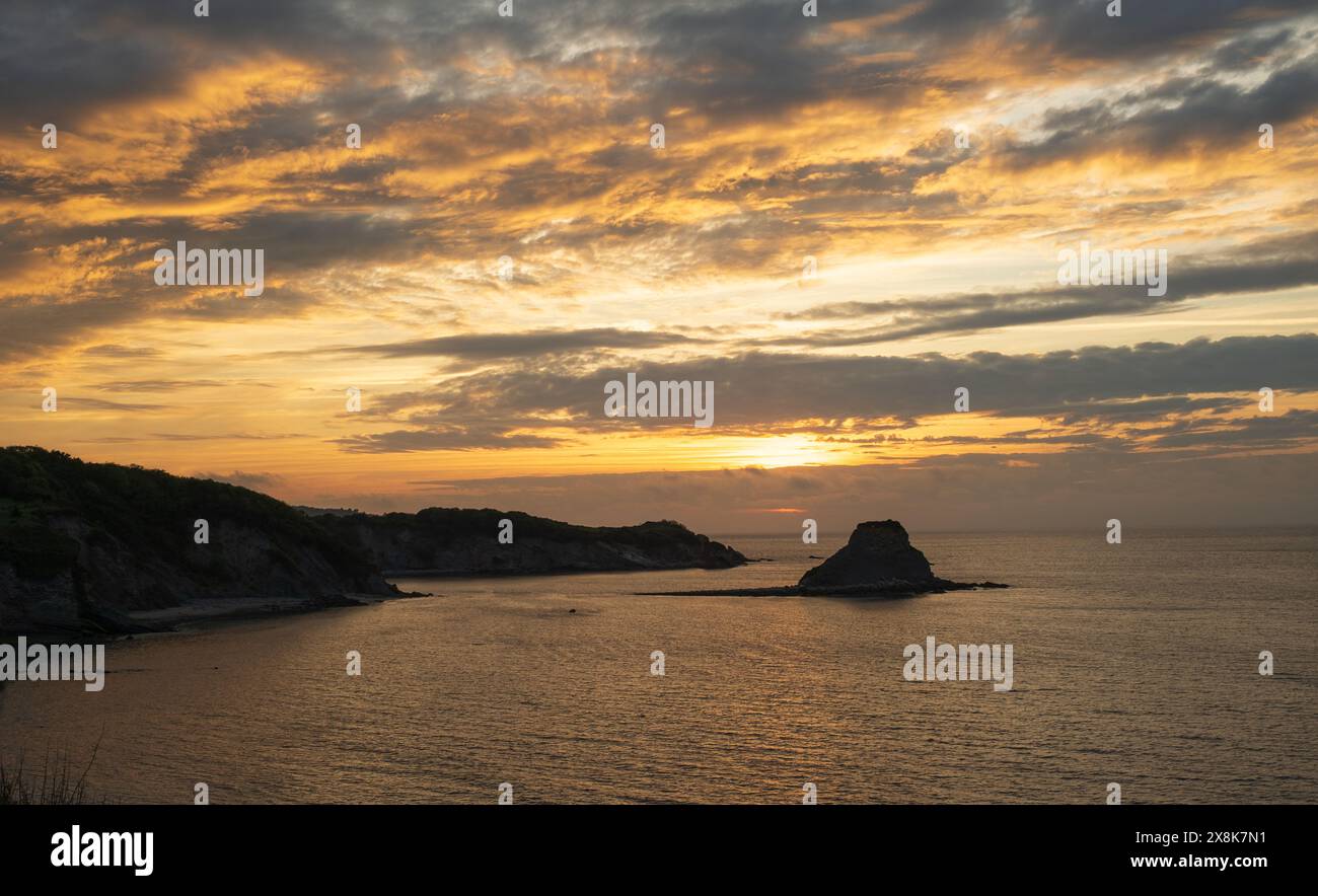 Panorama eines Sommersonnenuntergangs in der Bucht, Sie können sehen, wie sich die Sonne hinter einigen Wolken versteckt und warme Farben am Himmel und im Meer hinterlässt. Sie können auch sehen Stockfoto