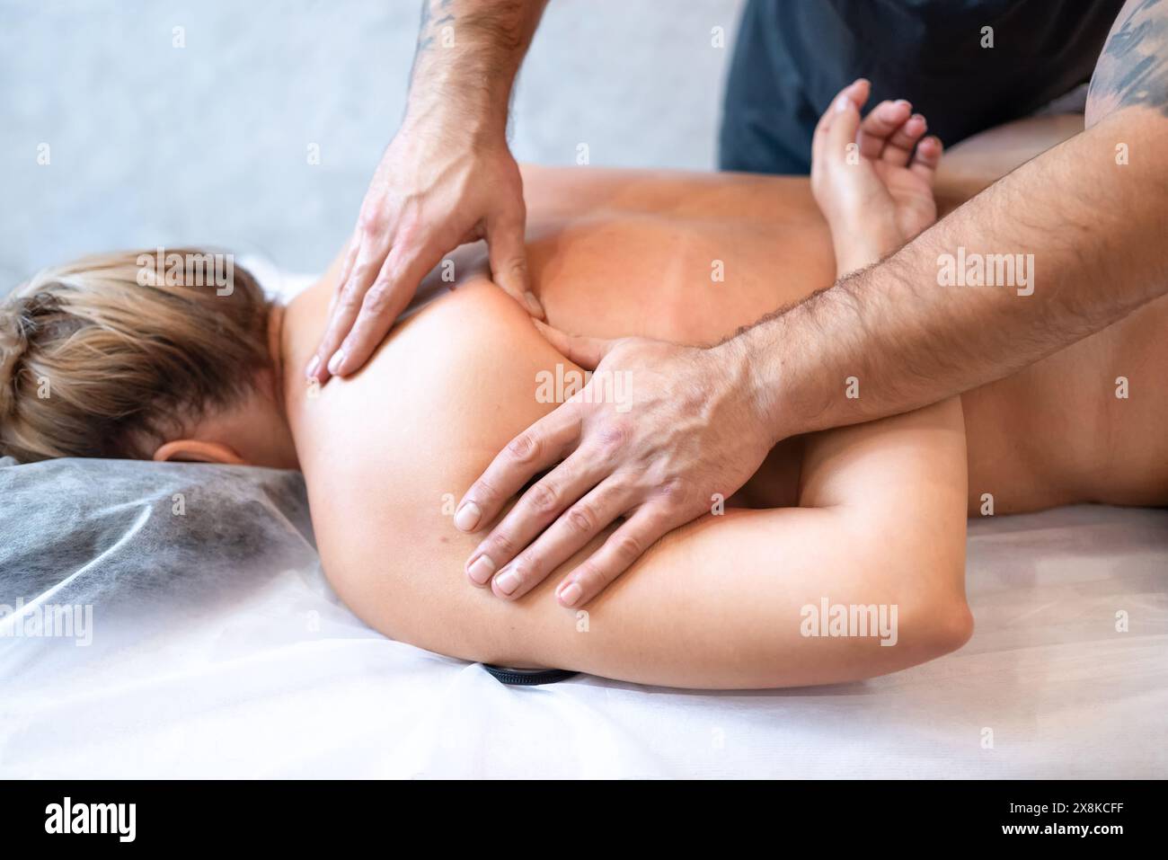 Der männliche Masseur massiert die Rücken- und Schulterblätter der Frau, die auf einem Massagetisch auf hellem Hintergrund liegt. Das Konzept der Massagebehandlungen. Stockfoto