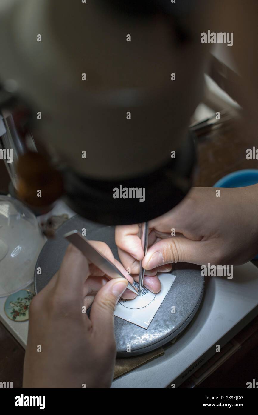 (240526) -- PEKING, 26. Mai 2024 (Xinhua) -- Ein Handwerker macht Jingtailan-Muster auf einem Zifferblatt unter einem Mikroskop in der Pekinger Enamel Factory in Peking, Hauptstadt Chinas, 15. Mai 2024. Während der Yuan-Dynastie (1271–1368) aus den arabischen Ländern eingeführt und in den Jingtai-Jahren der Ming-Dynastie (1368–1644) populär geworden, stellt Jingtailan eine spezielle lokale Cloisonne aus Kupfer und Porzellan dar. Mit Mustern, die mit Kupferdrähten strukturiert und mit Emailglasur lackiert sind, werden Dutzende von Verfahren, einschließlich Brennen, Schleifen und Vergoldung, auf mA angewendet Stockfoto