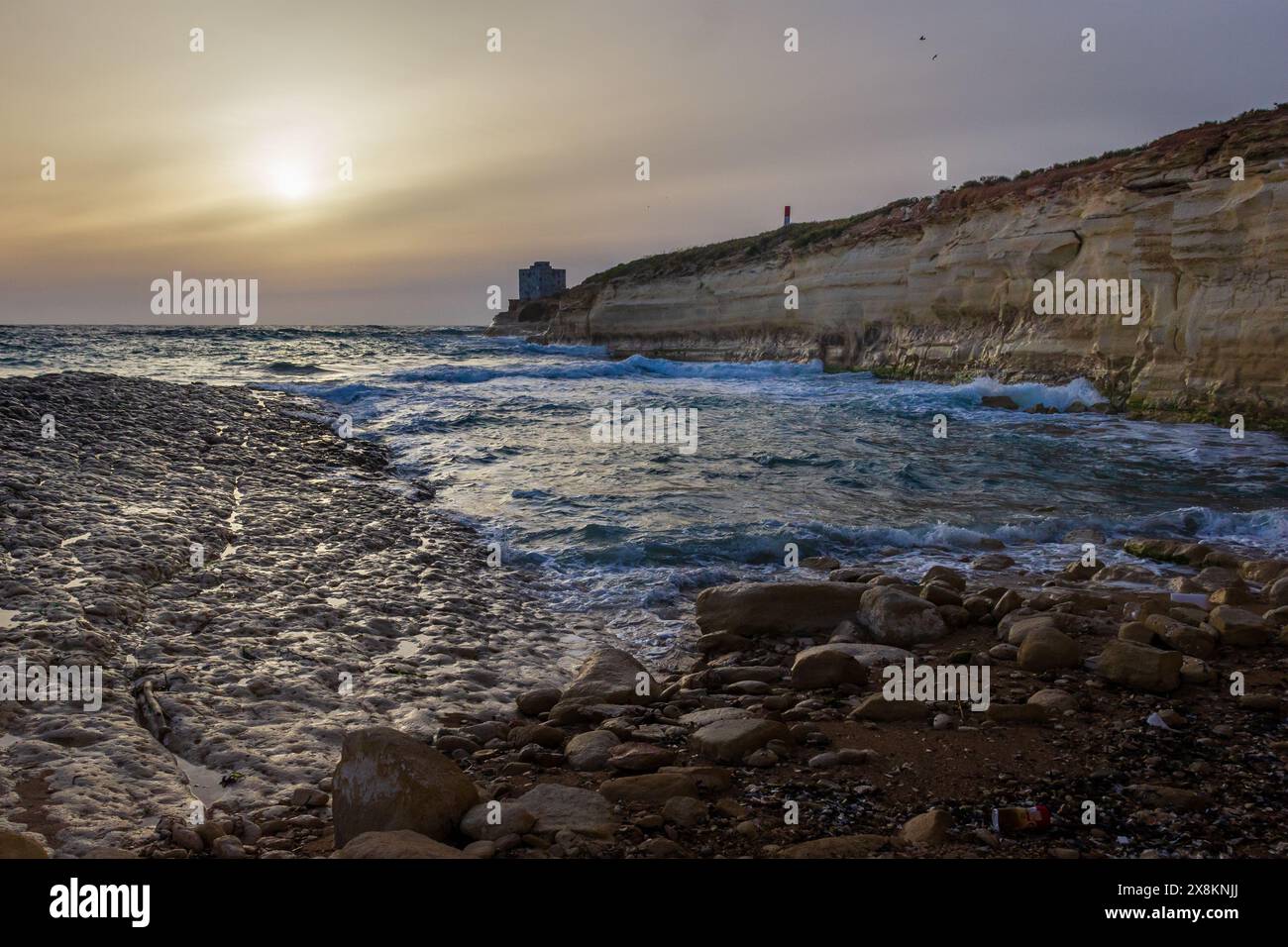 Die Sonne geht über dem Horizont auf und erleuchtet eine atemberaubende Strandlandschaft; die friedlichen Meereswellen stürzen gegen die felsigen Klippen der Küste. Stockfoto