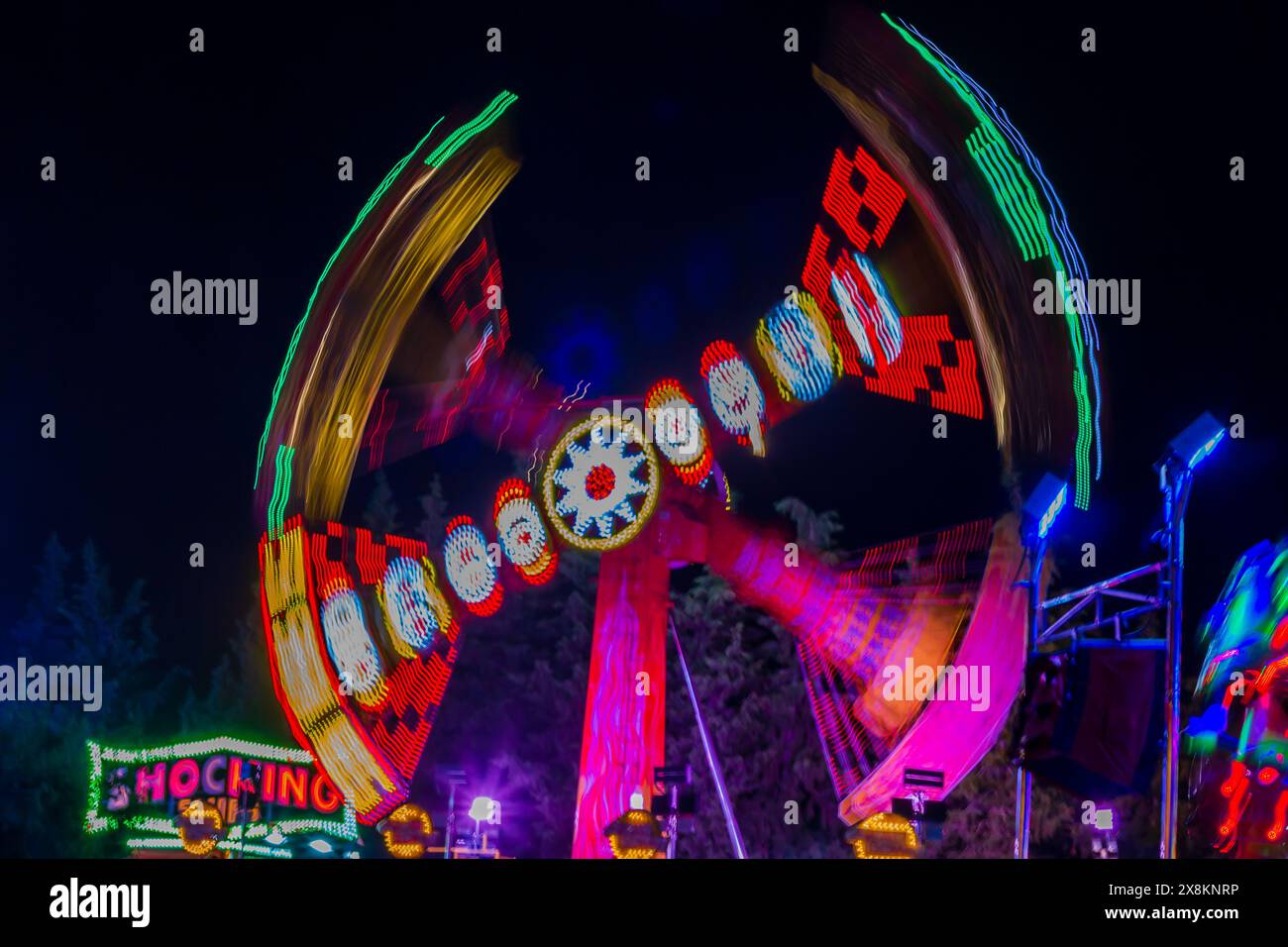 Ein mehrfarbiges Riesenrad beleuchtet den Nachthimmel bei Langzeitbelichtung. Stockfoto