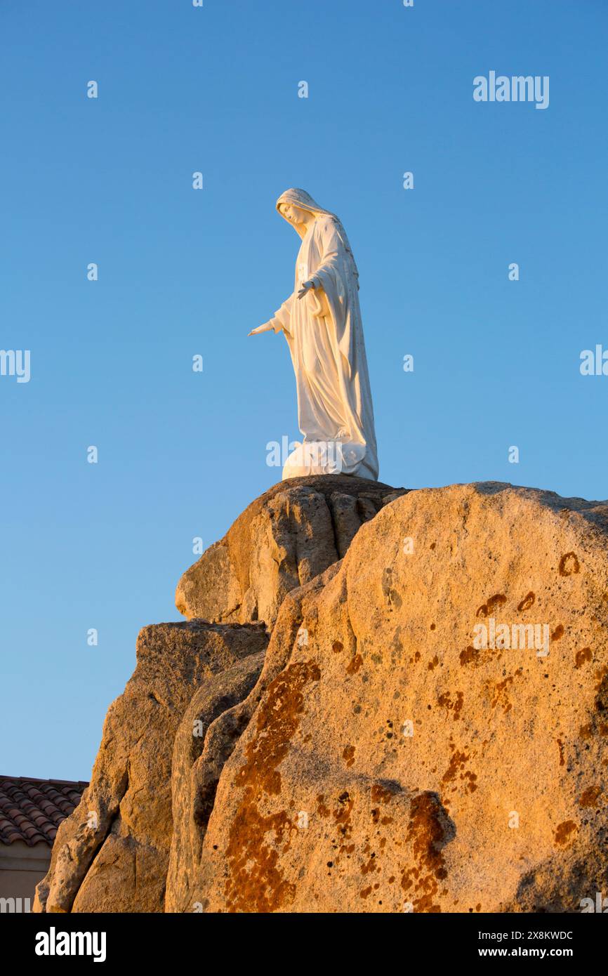 Calvi, Haute-Corse, Korsika, Frankreich. Imposante Statue der Jungfrau Maria auf felsigem Felsvorsprung an der Chapelle Notre Dame de la Serra, Sonnenaufgang. Stockfoto