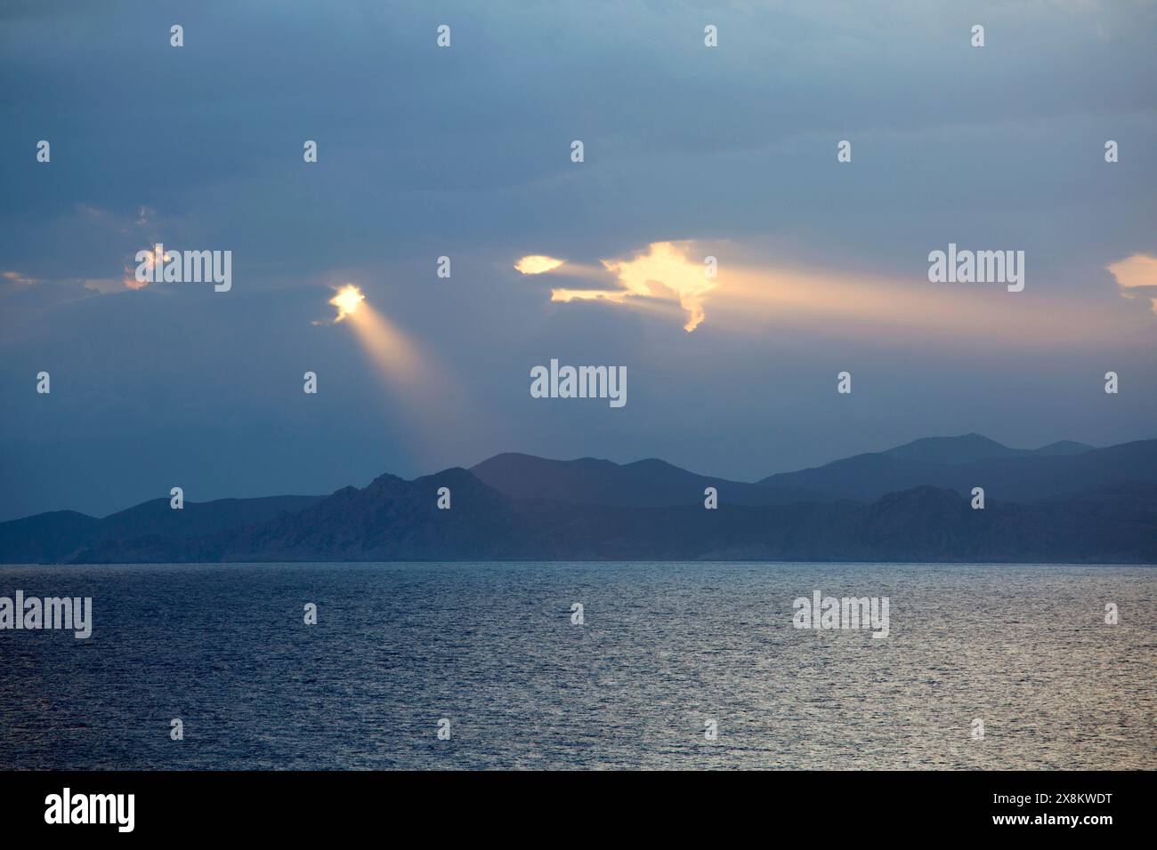 L’Ile-Rousse, Haute-Corse, Korsika, Frankreich. Rosafarbene Wellen der frühen Morgensonne, die durch dunkle Wolken über dem Désert des Agriates scheint. Stockfoto