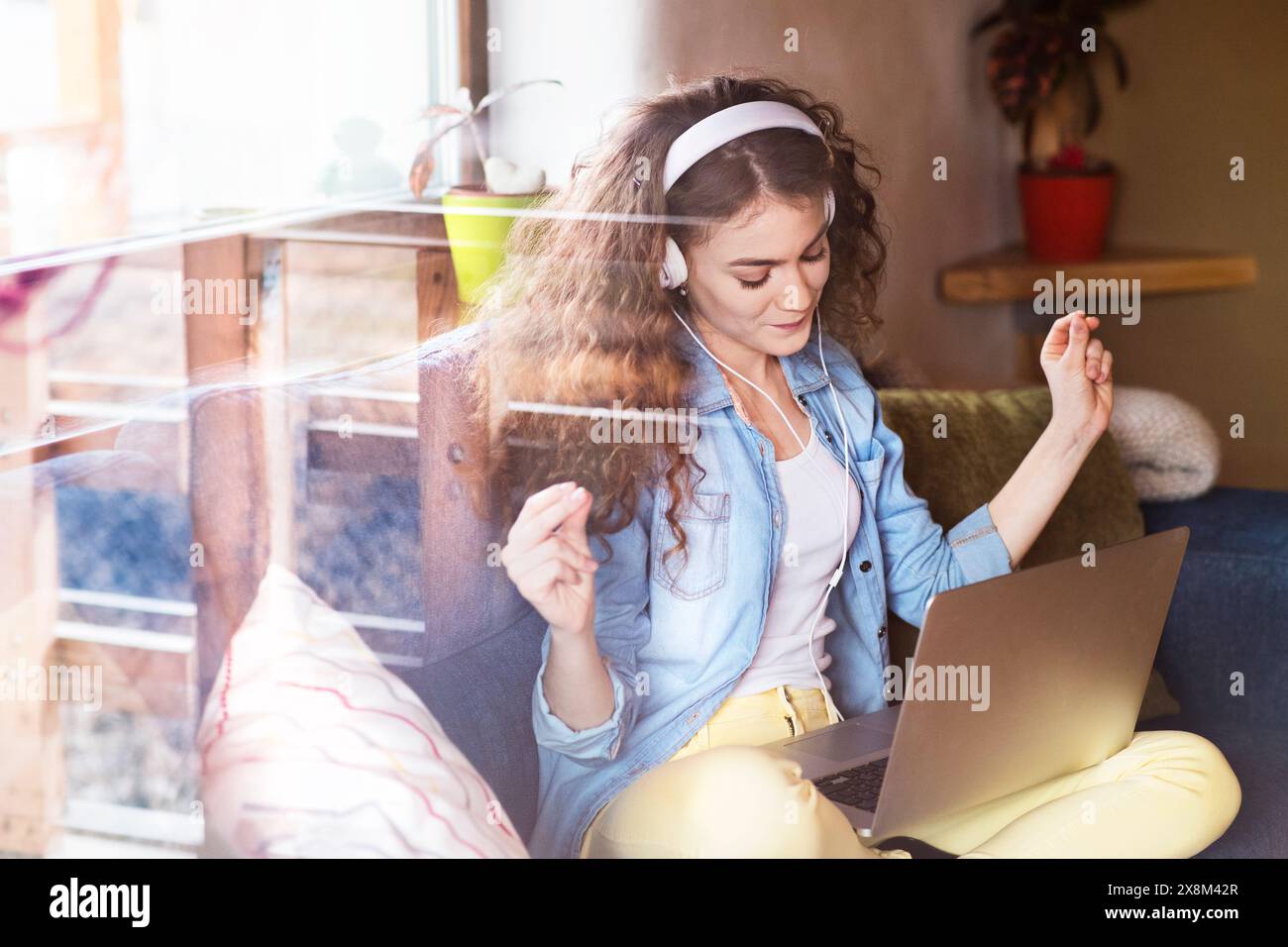 Schöne Frau mit lockigem Haar, die Kopfhörer trägt, Musik hört, positive Affirmationen. Stockfoto
