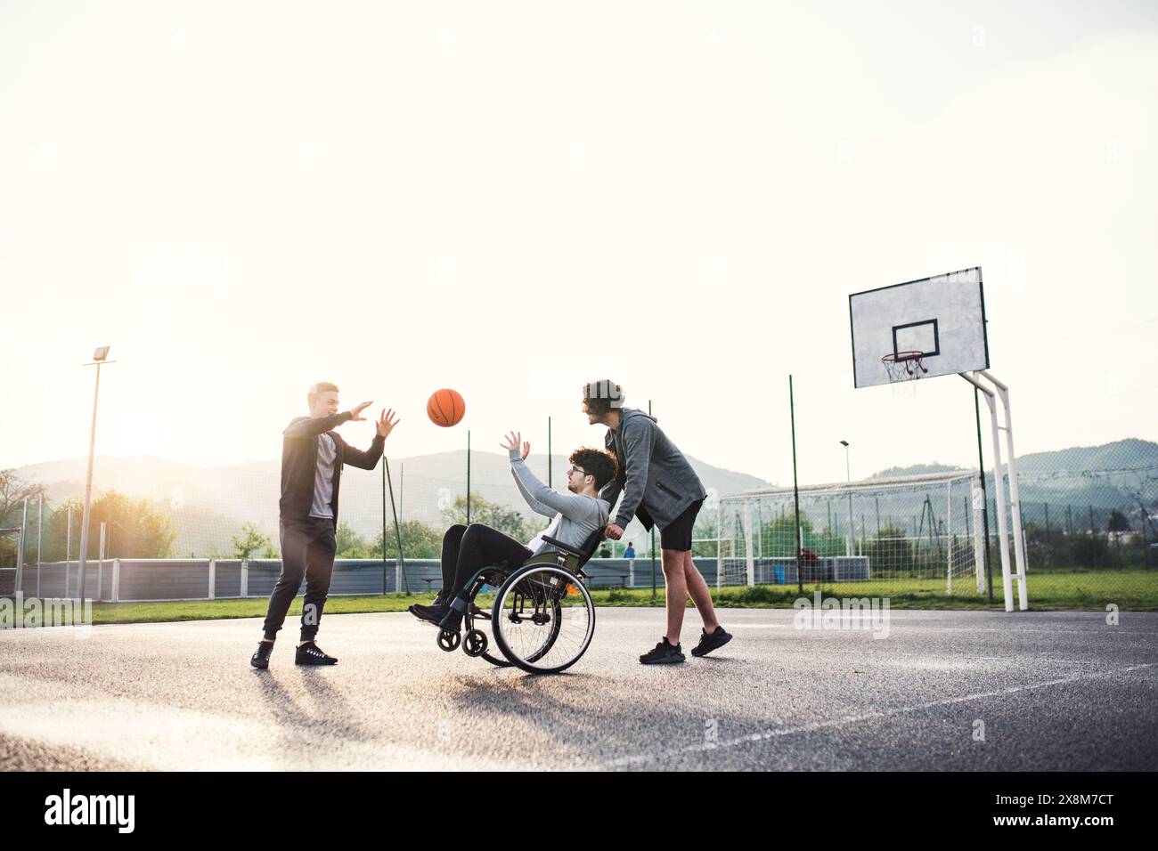 Behinderter junger Mann im Rollstuhl, der mit seinen Freunden Basketball spielt. Teamwrok und männliche Freundschaft. Stockfoto